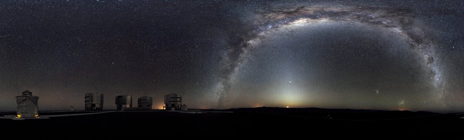 The Milky Way arches across this 360-degree panorama of the night sky above the Paranal platform, home of ESO’s Very Large Telescope. The Moon is just rising and the zodiacal light shines above it, while the Milky Way stretches across the sky opposite the observatory. To the right in the image and below the arc of the Milky Way, two of our galactic neighbors, the Small and Large Magellanic Clouds, can be seen. The open telescope domes of the world’s most advanced ground-based astronomical observatory are all visible in the image: the four smaller 1.8-metre Aŭiliary Telescopes that can be used together in the interferometric mode, and the four giant 8.2-metre Unit Telescopes. The image was made from 37 individual frames with a total exposure time of about 30 minutes, taken in the early morning hours.