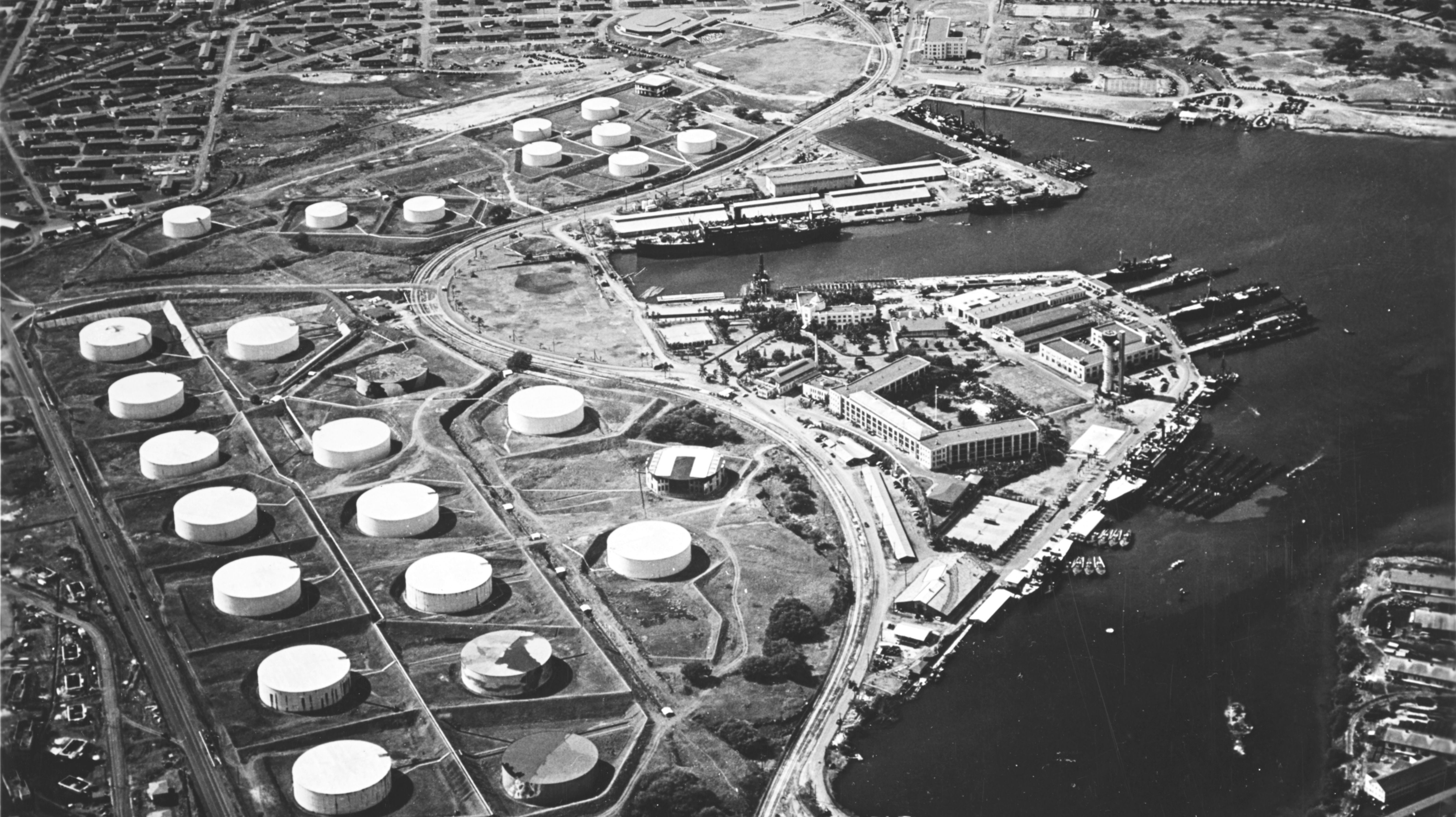 Aerial view of the Pearl Harbor submarine base (right center) with the fuel farm at left, looking south on 13 October 1941.
Among the 16 fuel tanks in the lower group and ten tanks in the upper group are two that have been painted to resemble buildings (topmost tank in upper group, and rightmost tank in lower group). Other tanks appear to be painted to look like terrain features.

Alongside the wharf in right center are USS Niagara (PG-52) with seven or eight PT boats alongside (nearest to camera) and USS Holland (AS-3) with seven submarines alongside. About six more submarines are at the piers at the head of the submarine base peninsula.