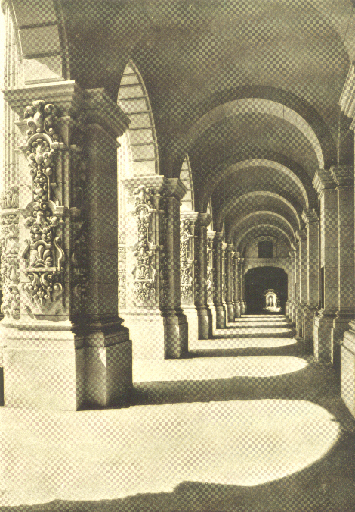 United States Building, the arcade — at the Panama-California Exposition, Balboa Park, San Diego, California.  

The arcade of the Government Building, or Sacramento Valley Building, extends through the flanking pavilions and is connected with the adjoining buildings by arcades with vine-covered pergolas above.  Looking through the arcade towards the west gives to the visitor one of the best vistas in the Exposition.
Down a few steps, out between high, neatly trimmed hedges, the scene is stopped by a cross hedge growing close to a fountain niche containing a quaintly leering faun.