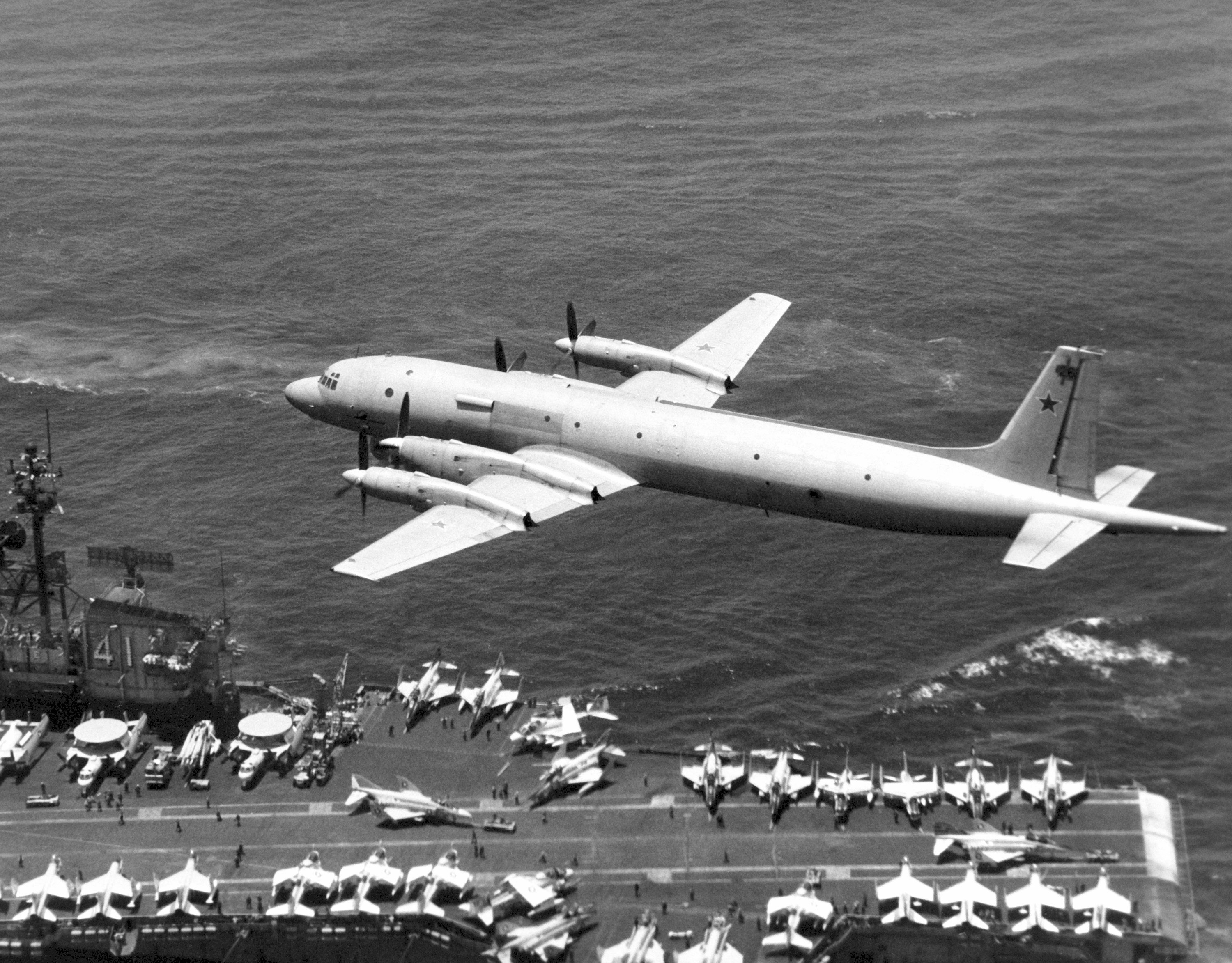 An air-to-air left rear view of a Soviet IL-38 May reconnaissance and anti-submarine warfare aircraft passing low over the flight deck of the aircraft carrier USS MIDWAY (CV 41).