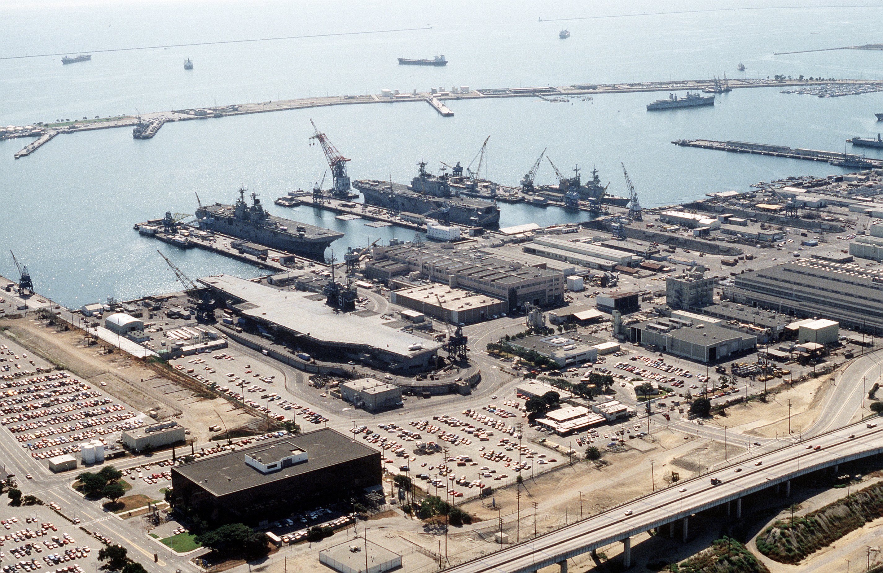 An aerial view of the decommissioned aircraft carrier USS Ranger (CV-61) in a graving dock at the shipyard Long Beach Naval Shipyard, California (USA), on 6 October 1993. Moored in the background are the amphibious assault ships USS Essex (LHD-2), left, and USS Tarawa (LHA-1), right.