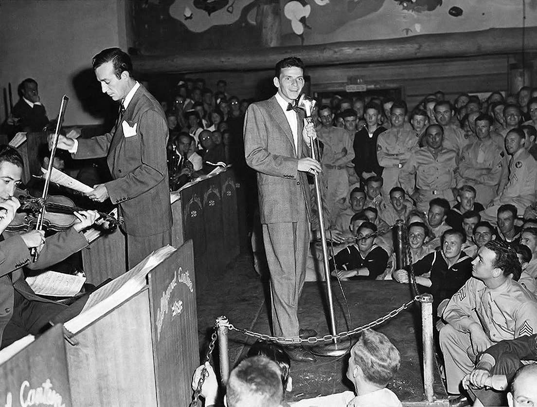 Publicity photo of Frank Sinatra (center) performing at the Hollywood Canteen for US servicemen during World War II, accompanied by Harry James (left, standing with sheet music) and his big band.