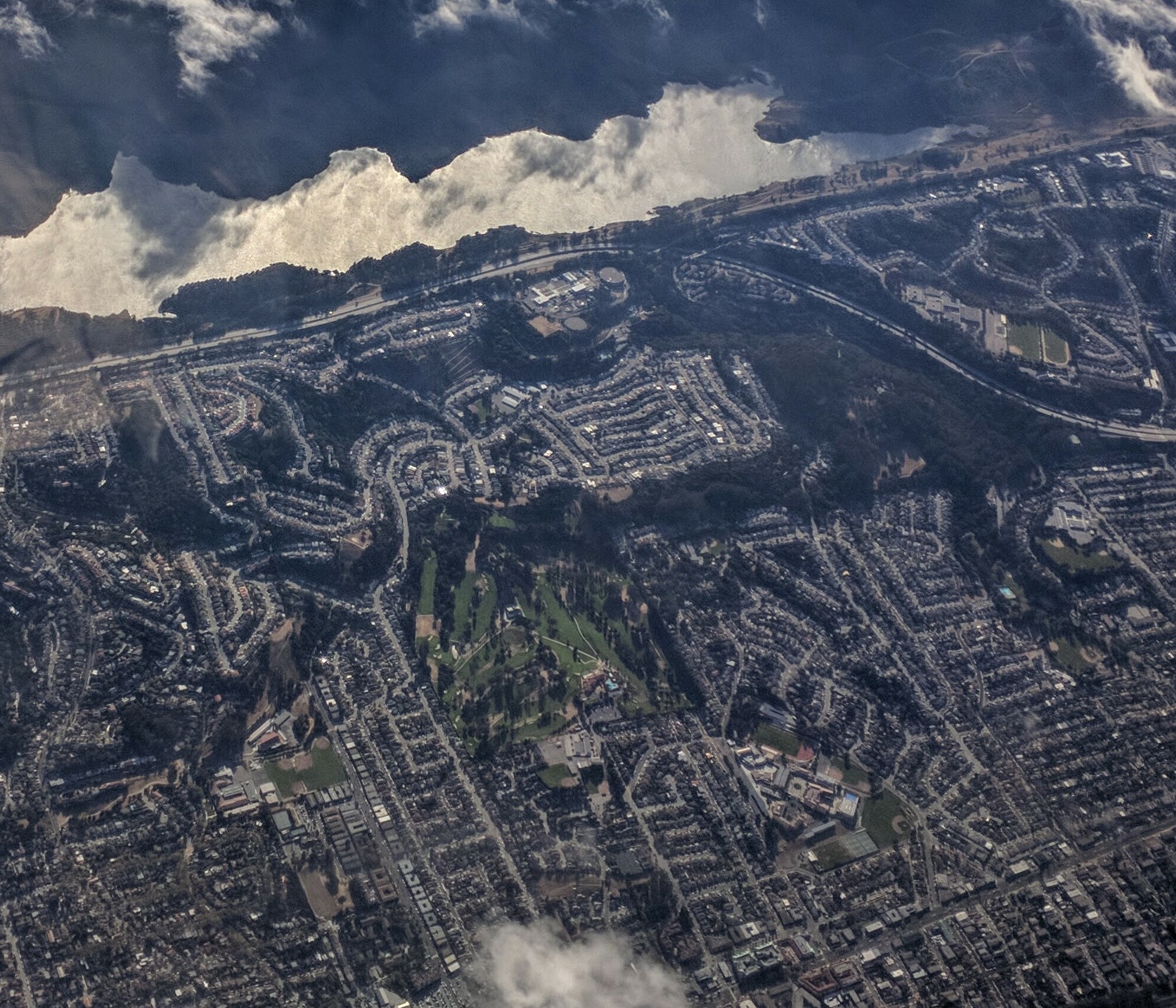 Aerial view of San Andreas Lake (body of water shown at top of image, lying west of Interstate 280) featuring parks (east of I-280) near Millbrae and San Bruno, California. The large, forested park closest to the freeway is Junipero Serra County Park. The green peninsula extending further east is San Bruno City Park, approximately in the center-right of the image. There is also a private golf course, the Green Hills Country Club, shown in the approximate center of the image.