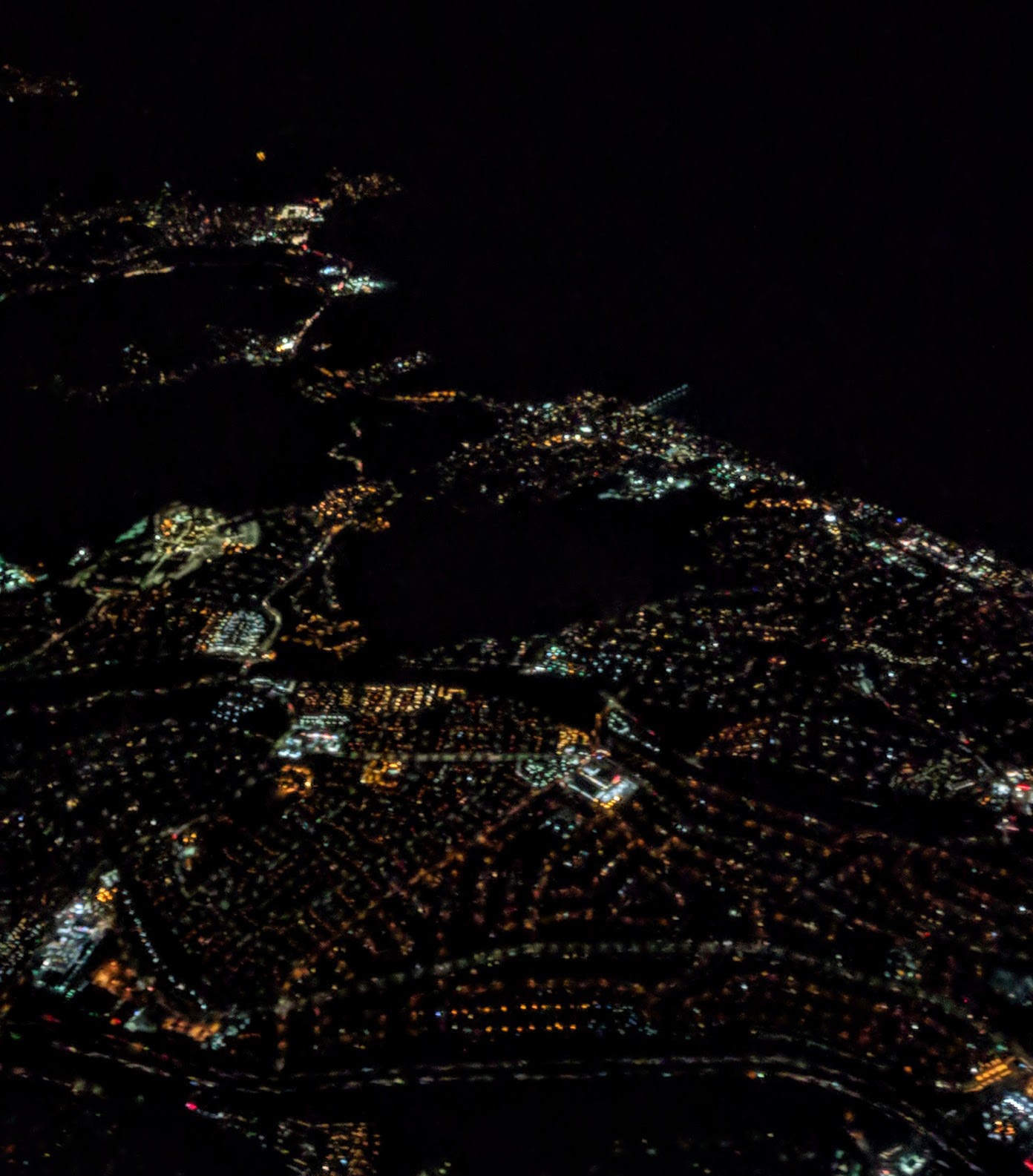 Night aerial view of the Pacific coast at Pacifica, California, and inland to California State Highway 35, Skyline Bldv.  The Pacific Pier is visible as a straight lighted feature sticking into the black ocean region at upper right.  The dark inland areas are open space, Milagra Ridge and Sweeney Ridge.