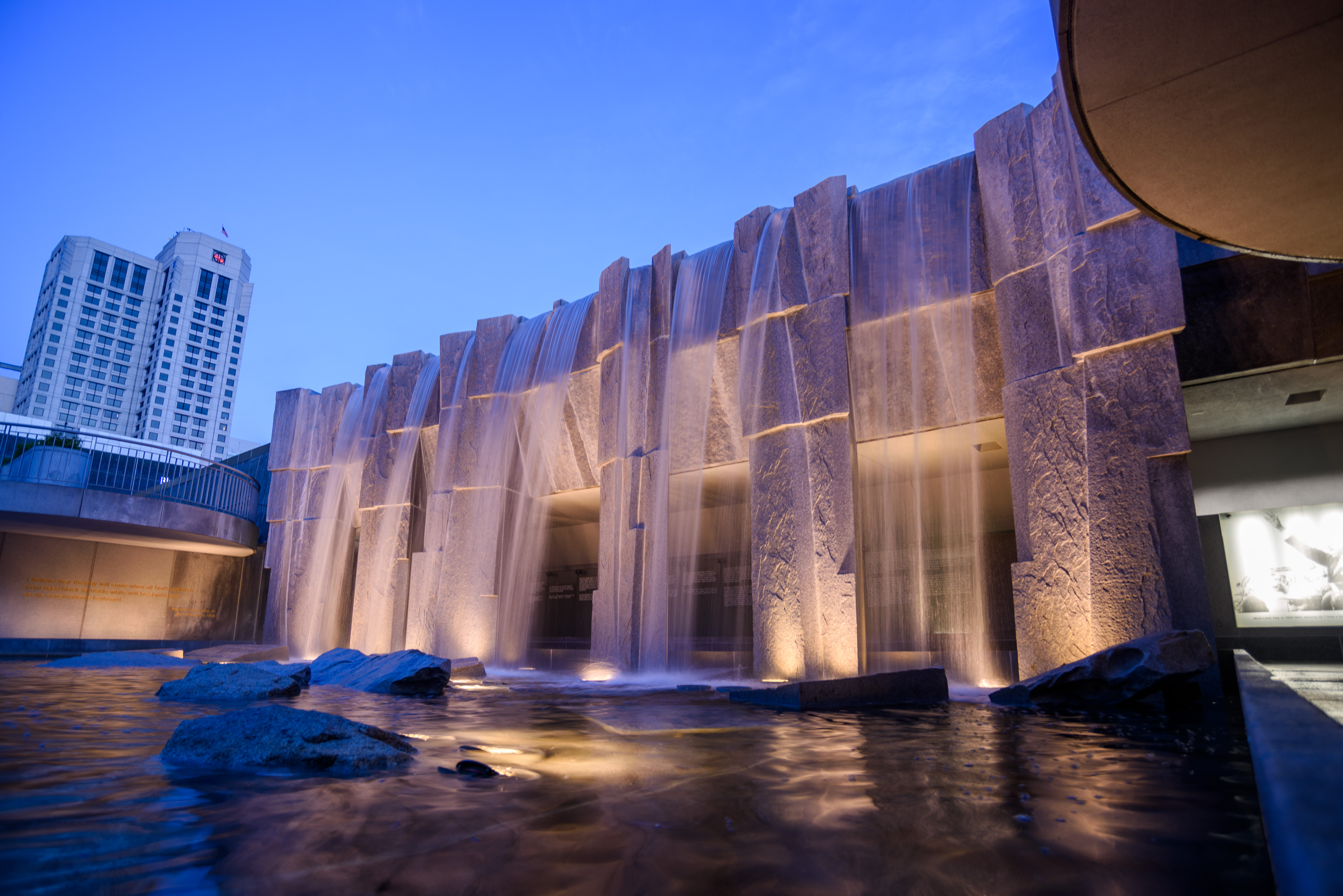 Lights below the surface of the water illuminate the waterfalls of the Martin Luther King, Jr. Memorial at twilight in Yerba Buena Gardens in San Francisco. Behind the waterfall are glass panels etched with quotes from MLK translated into several languages.