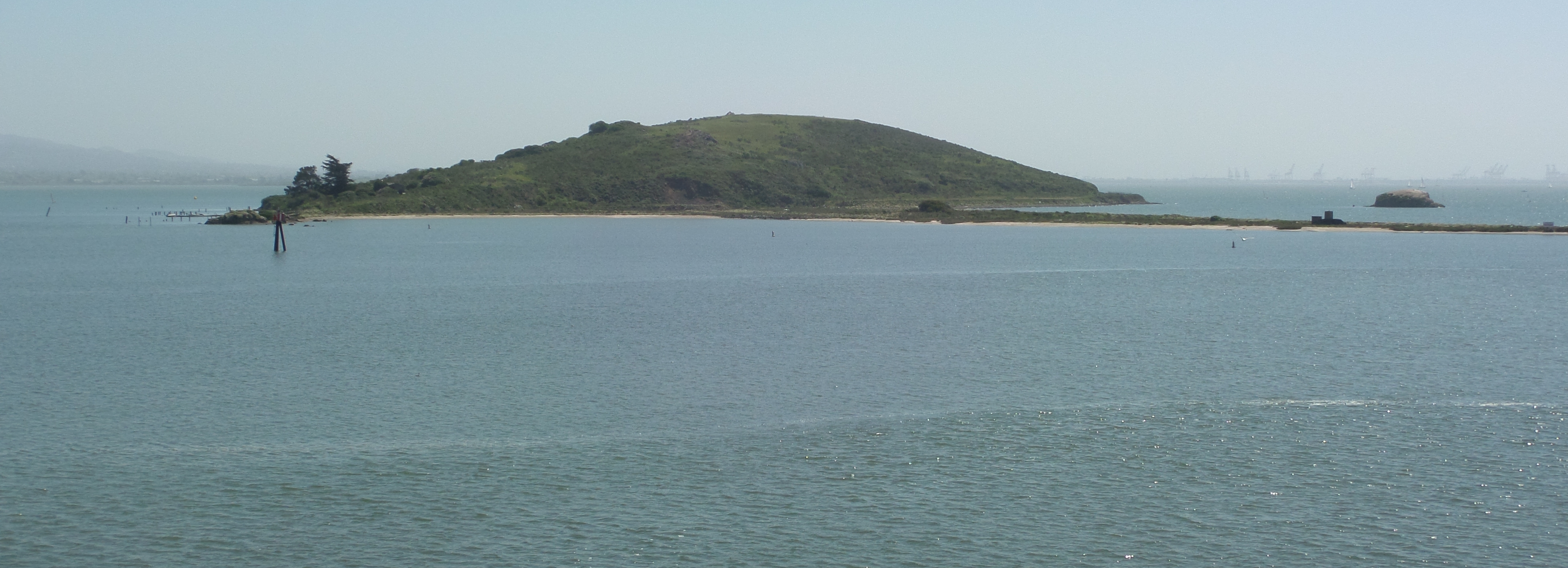 View of the main portion of en:Brooks Island, San Francisco Bay. To the right of the image can be seen the sandy spit that extends about 1 mile west of the main island. Beyond the spit is the small rock of Bird island. The cranes of the Port of Oakland can be seen in the distance. The photograph was taken looking southeast from the deck of the en:SS Red Oak Victory moored at Kaiser Shipyard No. 3, at Point Potrero in en:Richmond, California