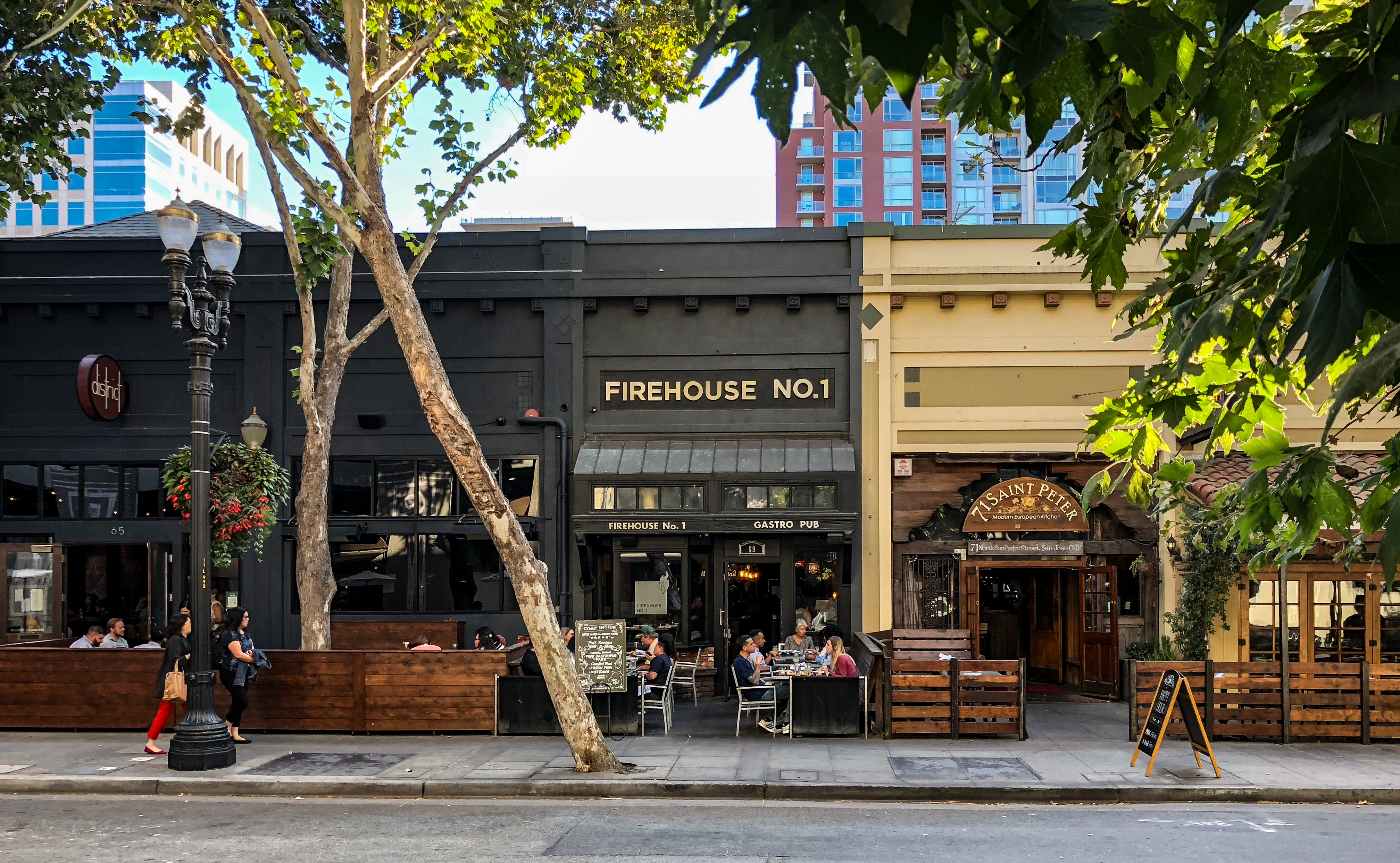 The Firehouse No. 1 gastro pub, a casual fine dining restaurant in Downtown San Jose's San Pedro Square in San Jose, California in the San Francisco Bay Area, on North San Pedro Street. To the right is 71 Saint Peter, a farm-to-table California European restaurant. On the left is the District Wine Whiskey and Cocktail bar. Patrons are dining at outdoor tables.