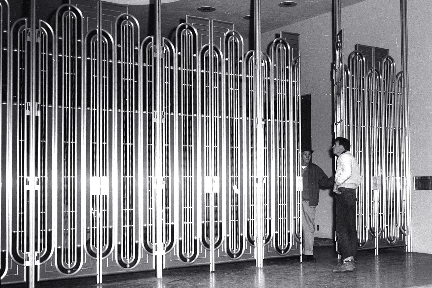 Entrance to Marin County Civic Center, 1963, with one visitor (white sweater) and a county employee. "Entrances are controlled by vertical grills of gold-anodized metal with rounded tops and bottoms, rather than doors."