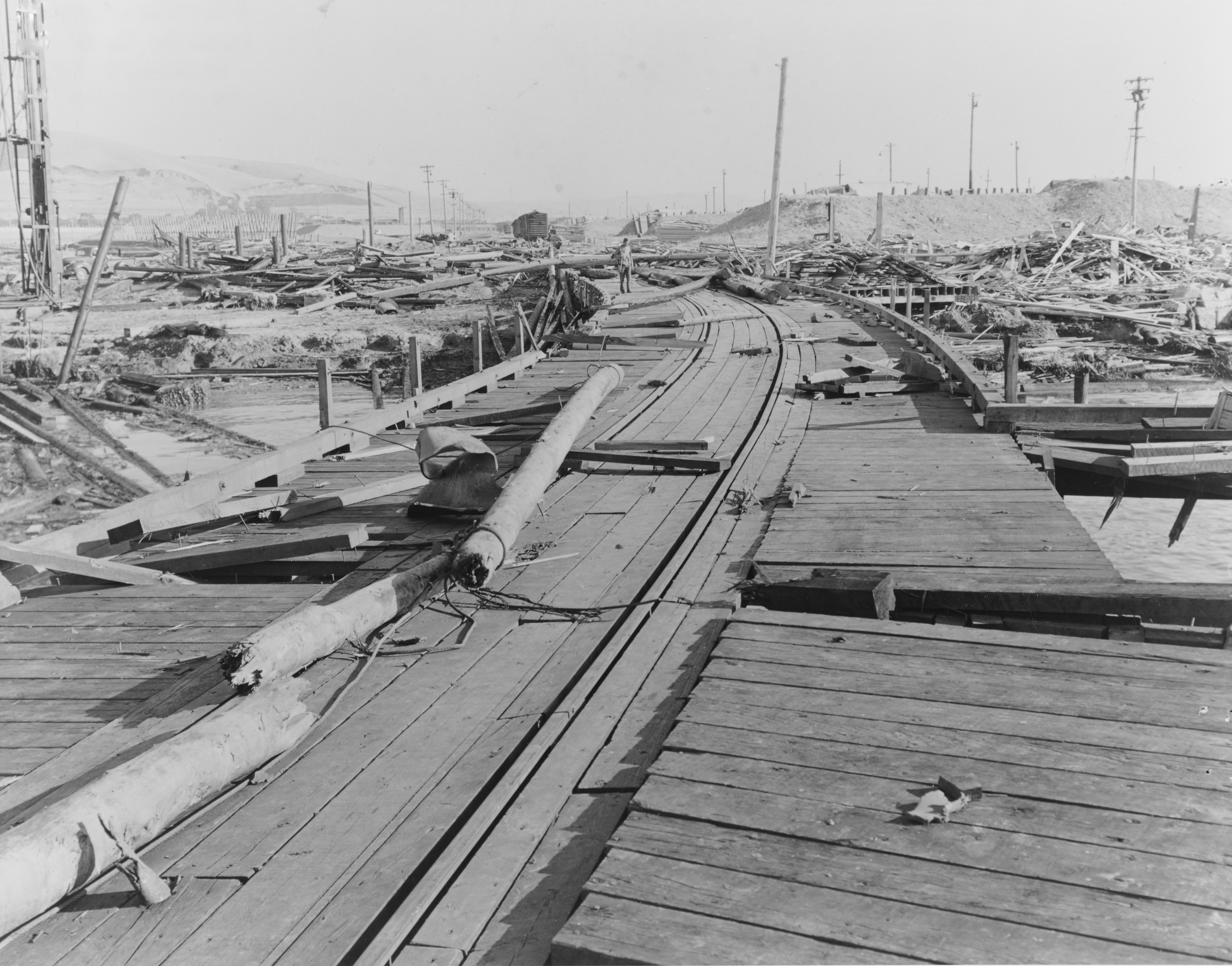 Naval Magazine, Port Chicago, California, damage resulting from the Port Chicago ammunition explosion disaster of July 17, 1944. From the source: "This view looks south from the Ship Pier, showing the wreckage of Building A-7 (Joiner Shop) at the right. There is a piece of twisted steel plating just to left of the long pole in left center."