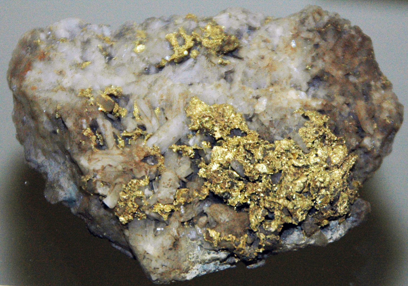 Gold on quartz from California, USA. (public display, Leadville Mining Museum, Leadville, Colorado, USA)
A mineral is a naturally-occurring, solid, inorganic, crystalline substrance having a fairly definite chemical composition and having fairly definite physical properties.  At its simplest, a mineral is a naturally-occurring solid chemical.  Currently, there are over 4900 named and described minerals - about 200 of them are common and about 20 of them are very common.  Mineral classification is based on anion chemistry.  Major categories of minerals are: elements, sulfides, oxides, halides, carbonates, sulfates, phosphates, and silicates.
Elements are fundamental substances of matter - matter that is composed of the same types of atoms.  At present, 118 elements are known (four of them are still unnamed).  Of these, 98 occur naturally on Earth (hydrogen to californium).  Most of these occur in rocks &amp; minerals, although some occur in very small, trace amounts.  Only some elements occur in their native elemental state as minerals.
To find a native element in nature, it must be relatively non-reactive and there must be some concentration process.  Metallic, semimetallic (metalloid), and nonmetallic elements are known in their native state as minerals.
Gold (Au) is the most prestigious metal known, but it's not the most valuable.  Gold is the only metal that has a deep, rich, metallic yellow color.  Almost all other metals are silvery-colored.  Gold is very rare in crustal rocks - it averages about 5 ppb (parts per billion).  Where gold has been concentrated, it occurs as wires, dendritic crystals, twisted sheets, octahedral crystals, and variably-shaped nuggets.  It most commonly occurs in hydrothermal quartz veins, disseminated in some contact- &amp; hydrothermal-metamorphic rocks, and in placer deposits.  Placers are concentrations of heavy minerals in stream gravels or in cracks on bedrock-floored streams.  Gold has a high specific gravity (about 19), so it easily accumulates in placer deposits.  Its high density allows prospectors to readily collect placer gold by panning.
In addition to its high density, gold has a high melting point (over 1000º C).  Gold is also relatively soft - about 2.5 to 3 on the Mohs Hardness Scale.  The use of pure gold or high-purity gold in jewelry is not desirable as it easily gets scratched.  The addition of other metals to gold to increase the hardness also alters the unique color of gold.  Gold jewelry made &amp; sold in America doesn’t have the gorgeous rich color of high-purity gold.

Locality: North Star Mine, Grass Valley Mining District, California, USA