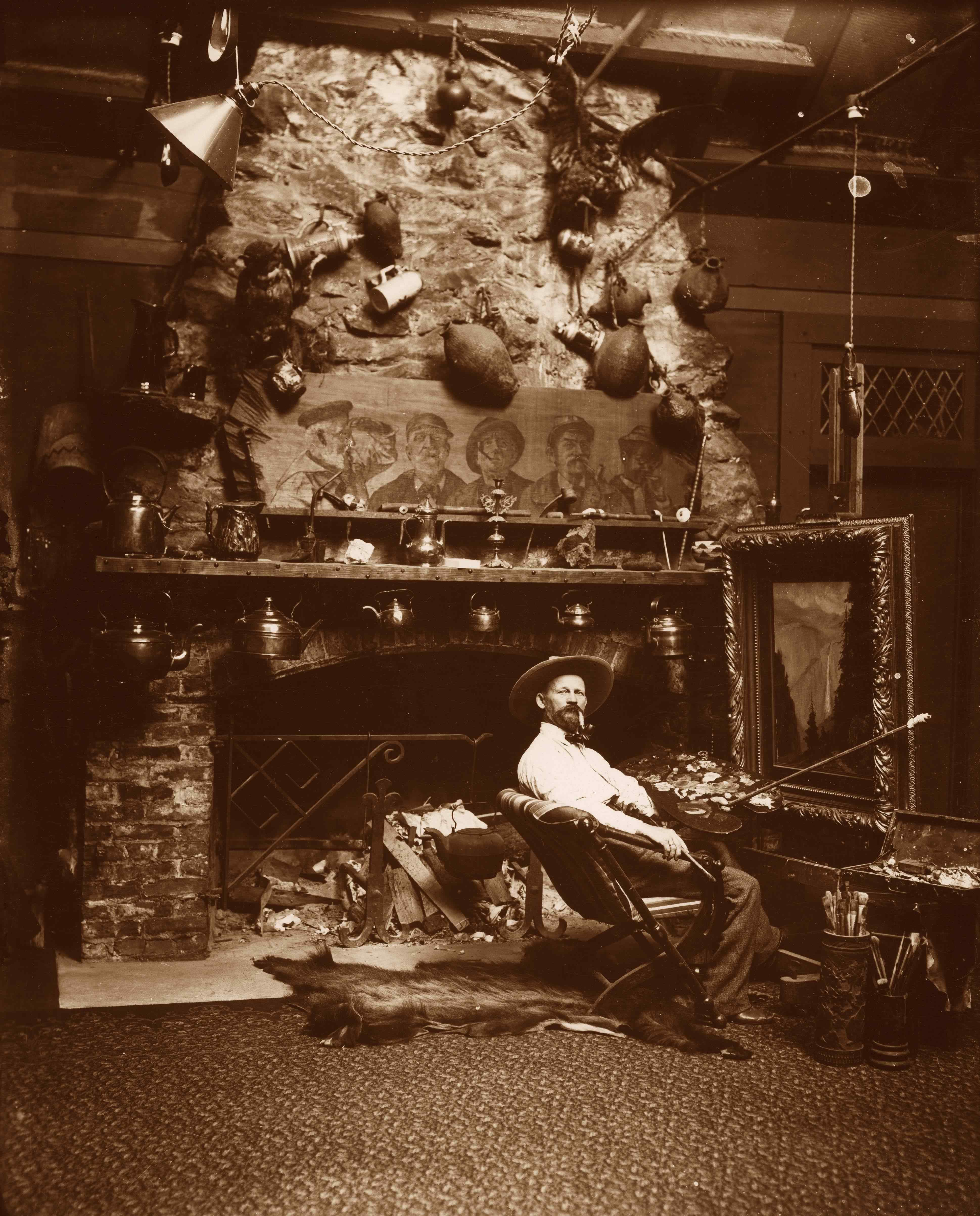 "6 1/2"" X 8 1/2""; GLASS NEGATIVES.
Yosemite Museum Collection 10243. Shows California artist Chris Jorgensen in his Yosemite studio in front of the fireplace--easel up in front of the chair he is sitting in--mantel of fireplace decorated with the figures of men and various size teakettles and mugs.
