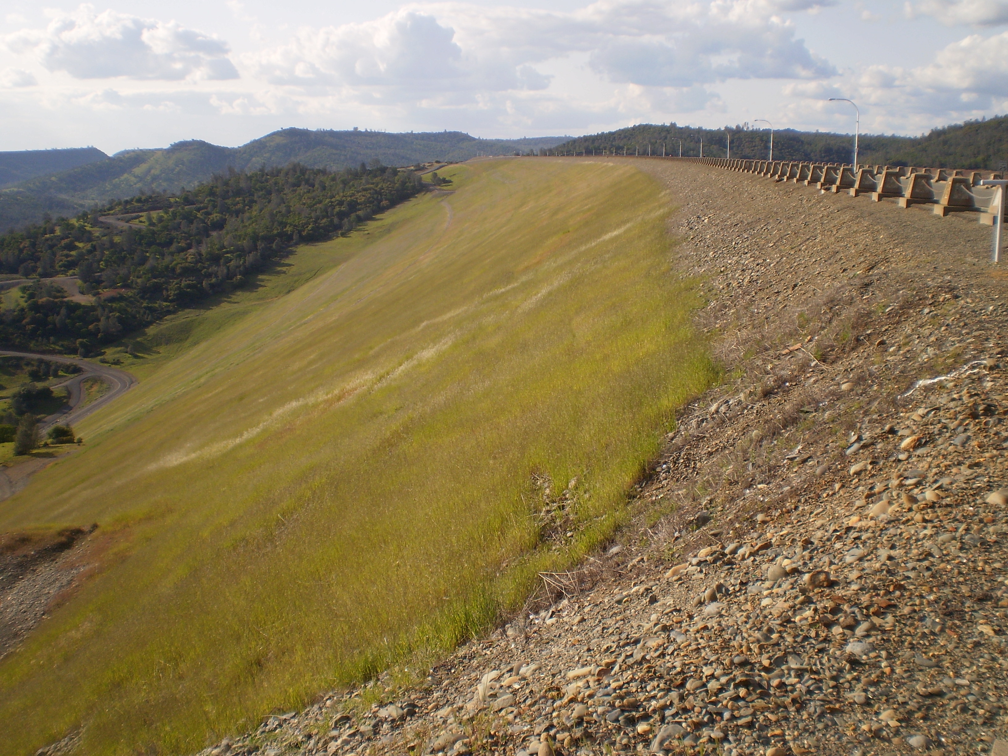 The face of Oroville Dam, an earth-filled embankment dam that impounds the Feather River to form Lake Oroville. The dam is located near Oroville, in Butte County, California. The photo shows the Sierra Nevada foothills in background.