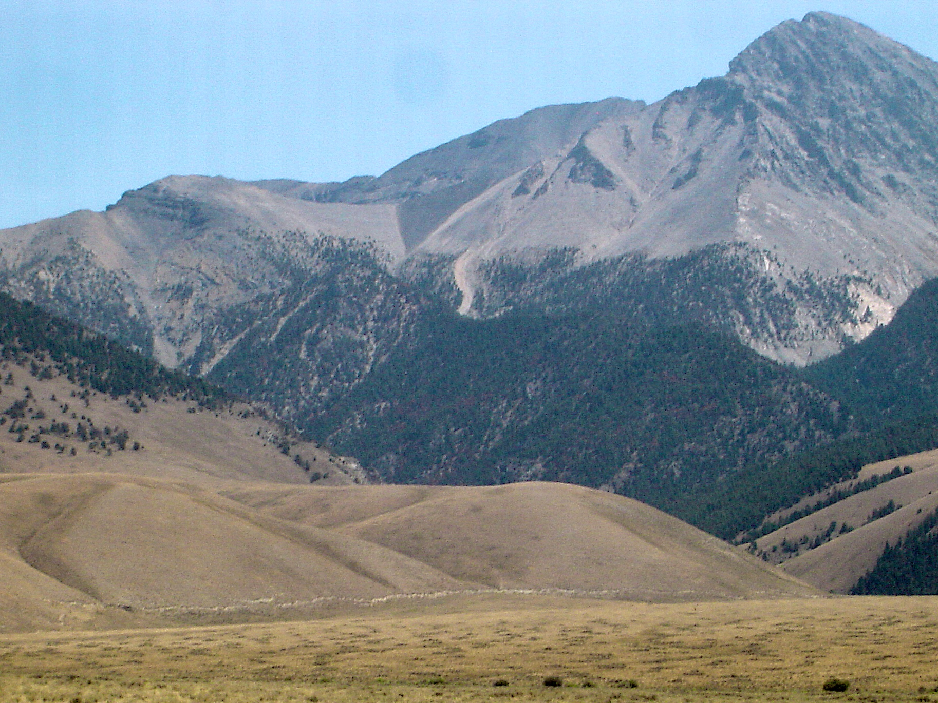 A picture of Borah Peak with the fault scarp from the 1983 Borah Peak earthquake shown as a line, near the base of the tan hill in the foreground.