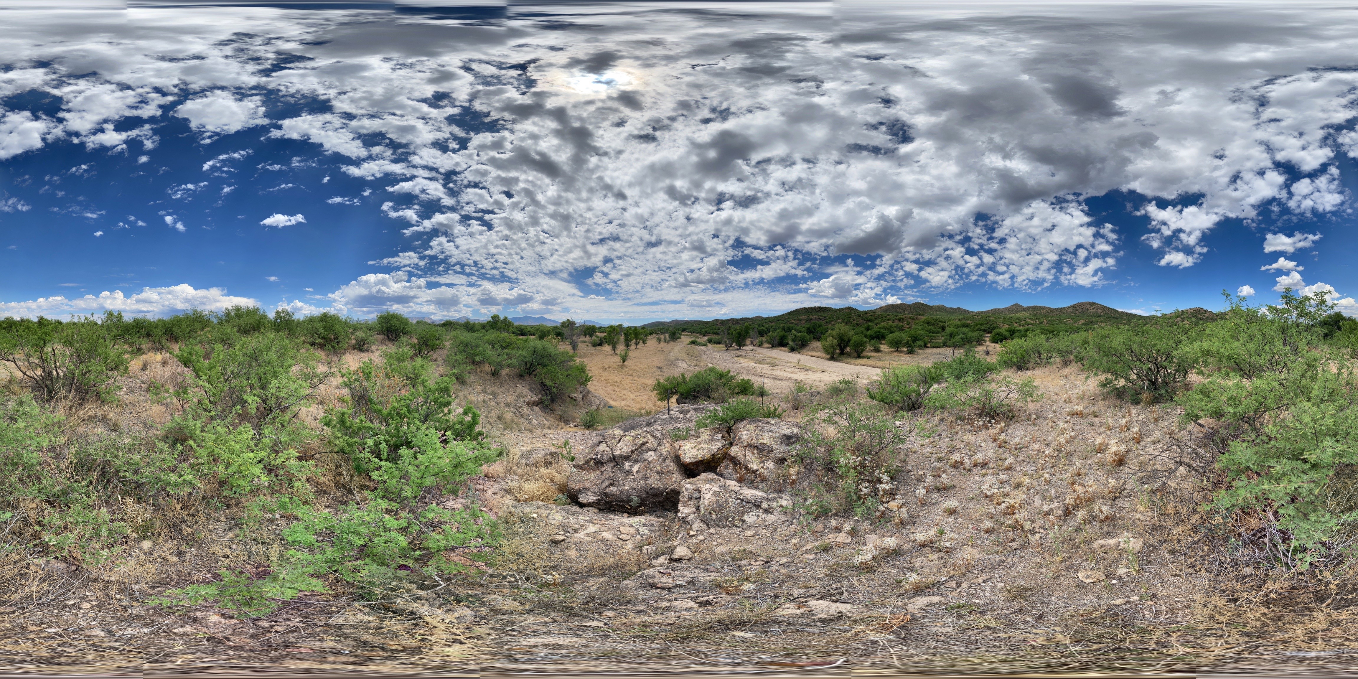 360 spherical panoramic photo of landscape with river bottom and floodplain below and blue sky with clouds above
Archeology reveals human settlement at the Guevavi site going back 4,000 years, likely due to its advantageous position along the Santa Cruz River. The underlying geology combined with rock outcrops on both sides of the river, create a pinch point for water to come to the surface. There were springs, irrigation ditches, and floodplain agriculture.