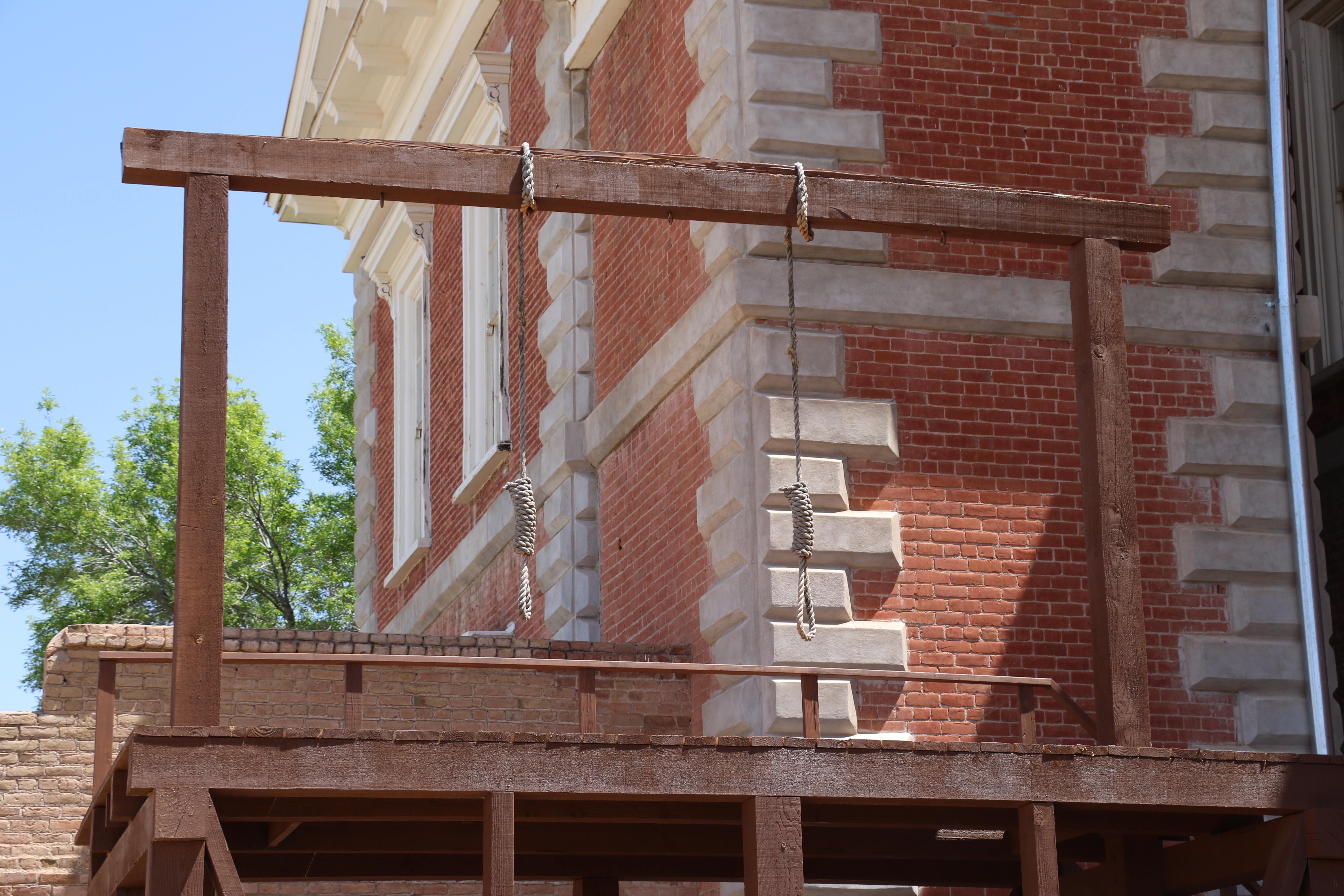 This 2017 reproduction gallows was built to more accurately represent the scale and position in the courtyard of the original used to hang five men in 1884 and two men in 1900. The original was burned in 1912. There are two nooses to represent the last use.