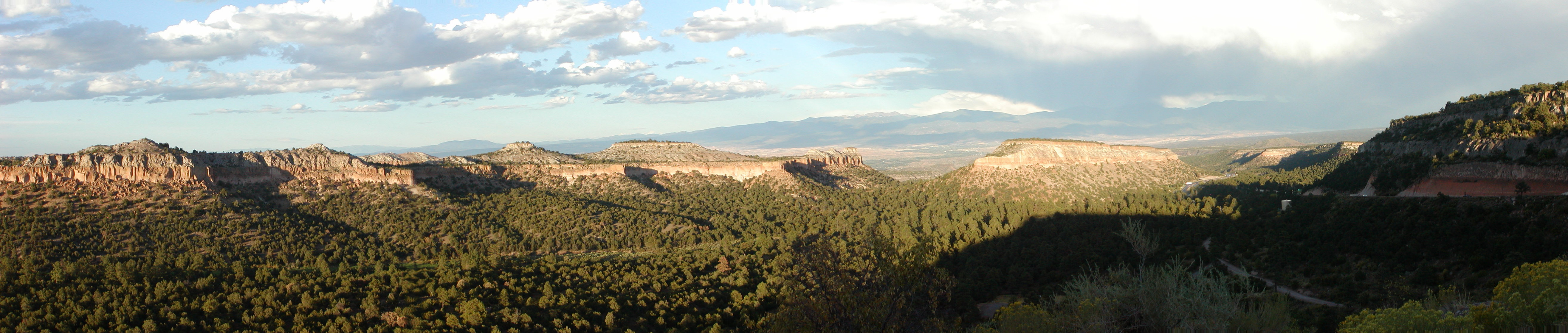 Panorama taken from Los Alamos Hill Road overlook. Photo taken on return from a solo canoe trip in Ontario, Canada cut short by 9/11 events. Taos is visible in the distance to the left, Espanola in the distance near center, Santa Fe is down valley to the right. Ottowi ruins and cliff dwellings are in the middle distance at left and center (cliff dwellings are visible as dark shadows at the base of the cliffs at the left). The main site can be seen in an expanded view as an area of light green on a gentle slope dropping to the left. The dark green areas in the picture are Pinon pines, most of which died from beetle damage in the droughts of subsequent years.
The photo was constructed from 4 individual hand-held shots using an Olympus C-700 UZ camera, and stitched using the native Olympus software package. Each of the 4 frames were 1600x1200, shot at f/4, 1/800 s, ISO 100. The size of the uploaded panorama file was 5260x1119.