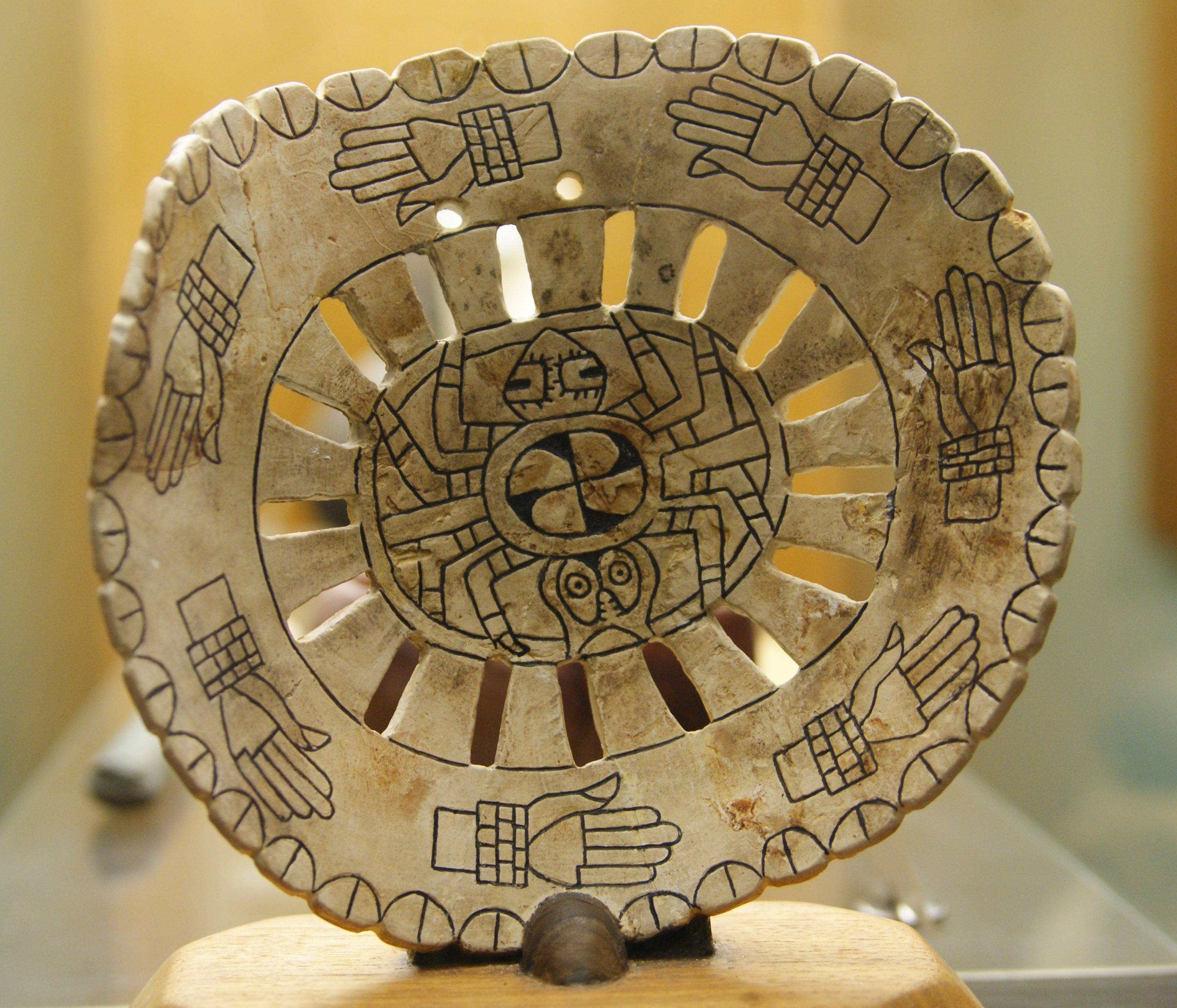 Spiro mound artifacts on display at Woolaroc Museum, near Bartlesville. Spider motif at center with circle of hands with shell bracelets. Roughly 3 in x 3 in.