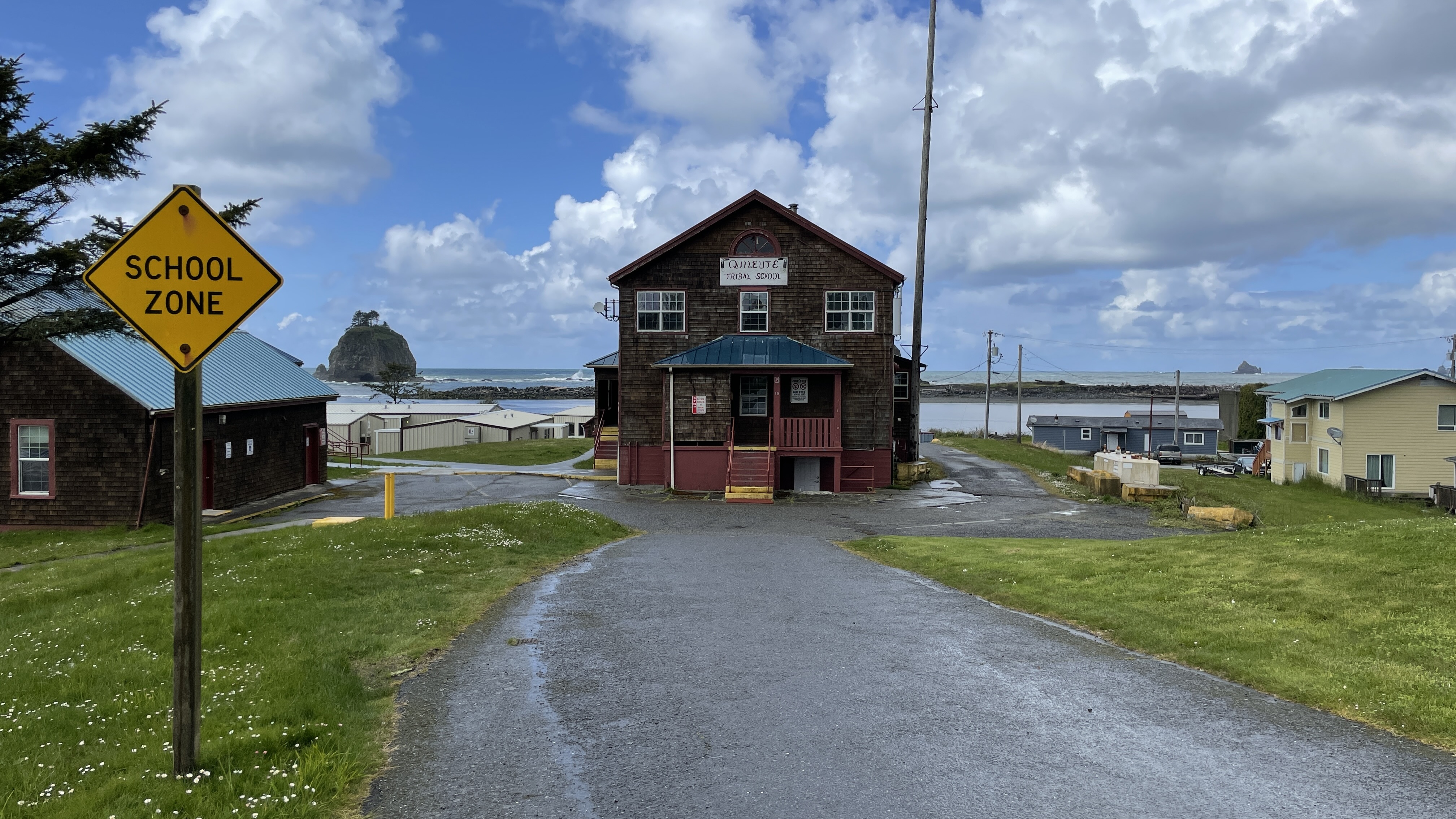 This building was originally constructed in 1931, as part of the Coast Guard facilities in La Push, Washington. In 1979, it was renovated for use as a schoolhouse. To the left, tops of portable buildings used as classrooms can be seen. The Quileute Tribal School now uses the old Coast Guard building as storage and office space.