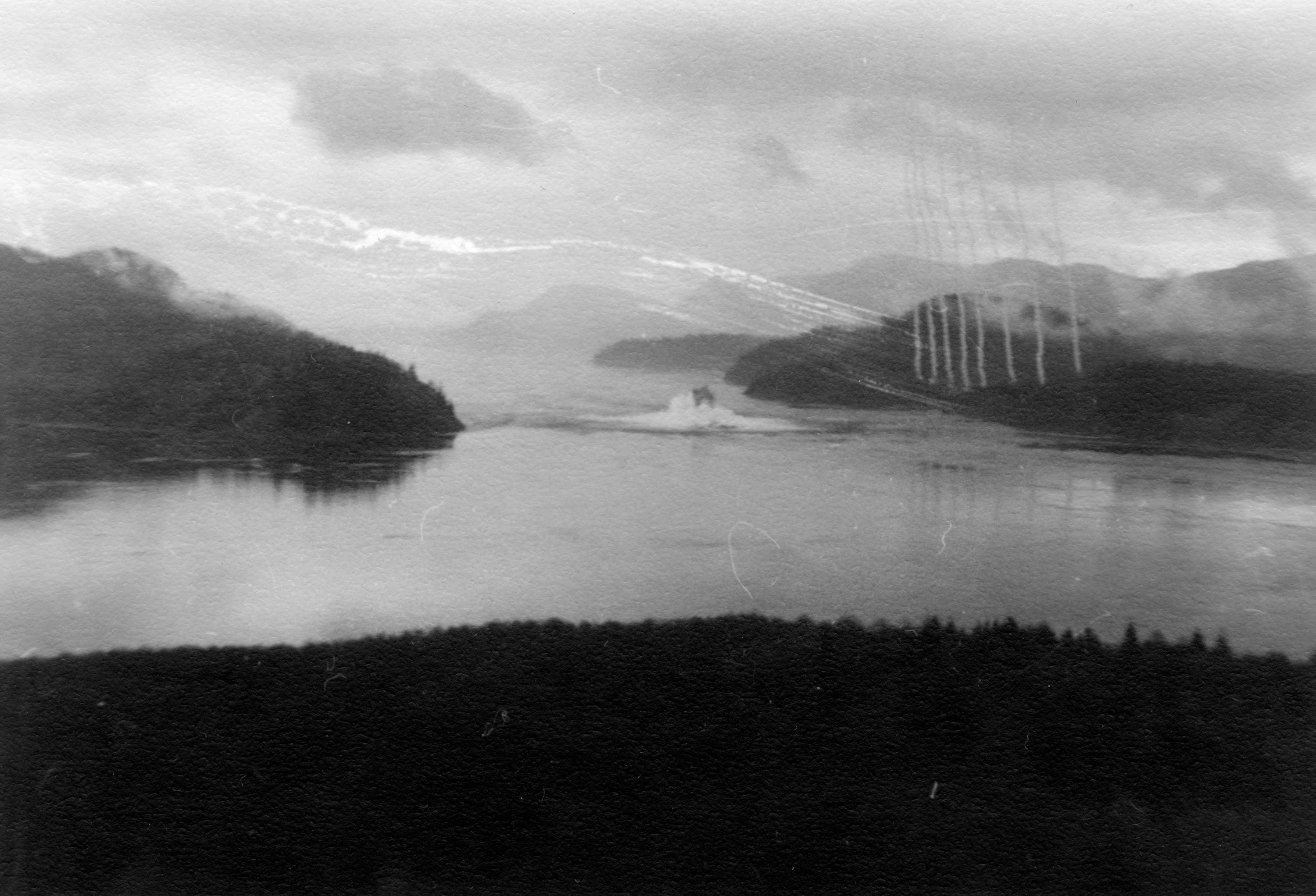 Item is a photograph of the blasting of Ripple Rock, the navigational hazard in the Seymour Narrows, from a bunker position on an area hilltop. This was taken immediately following detonation, with the blast cloud having just broken through the surface of the water.