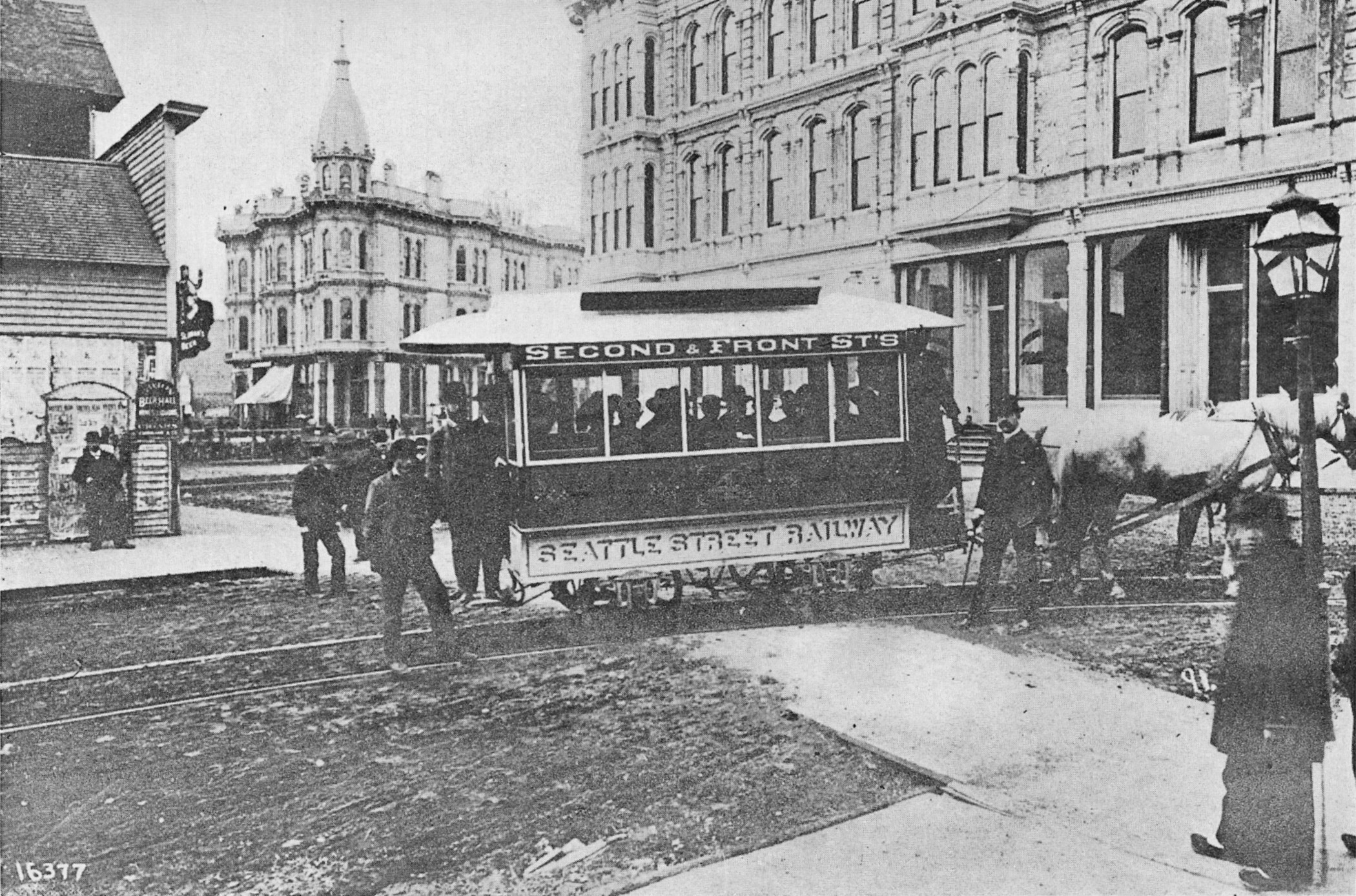 Description in the published source (1919):
First street car at Occidental Avenue and Yesler Way, about 1884. The view is across Pioneer Square. The building in the background stood on the present site of the Mutual Life Building at First Avenue and Yesler Way. The building on the right is a hotel. It was destroyed in the Great Fire and the Seattle Hotel Building now occupies this site. Mayor Leary and a party of invited guests are in the car.
The hotel in question was the Occidental Hotel. The Seattle Hotel on the same site was demolished in the 1960s. The Mutual Life Bilding, alluded to, is still at the corner of First and Yesler.
The tram is horse-drawn. Visible signs on the streetcar say "Second & Front St's", "Seattle Street Railway". In 1884, First Avenue would have been called Front Street and Occidental Avenue would have been called Second Street. The names were changed after the Great Seattle Fire (1889). Mayor Leary was John Leary, a business leader.
In the background at center is the Yesler-Leary Building.