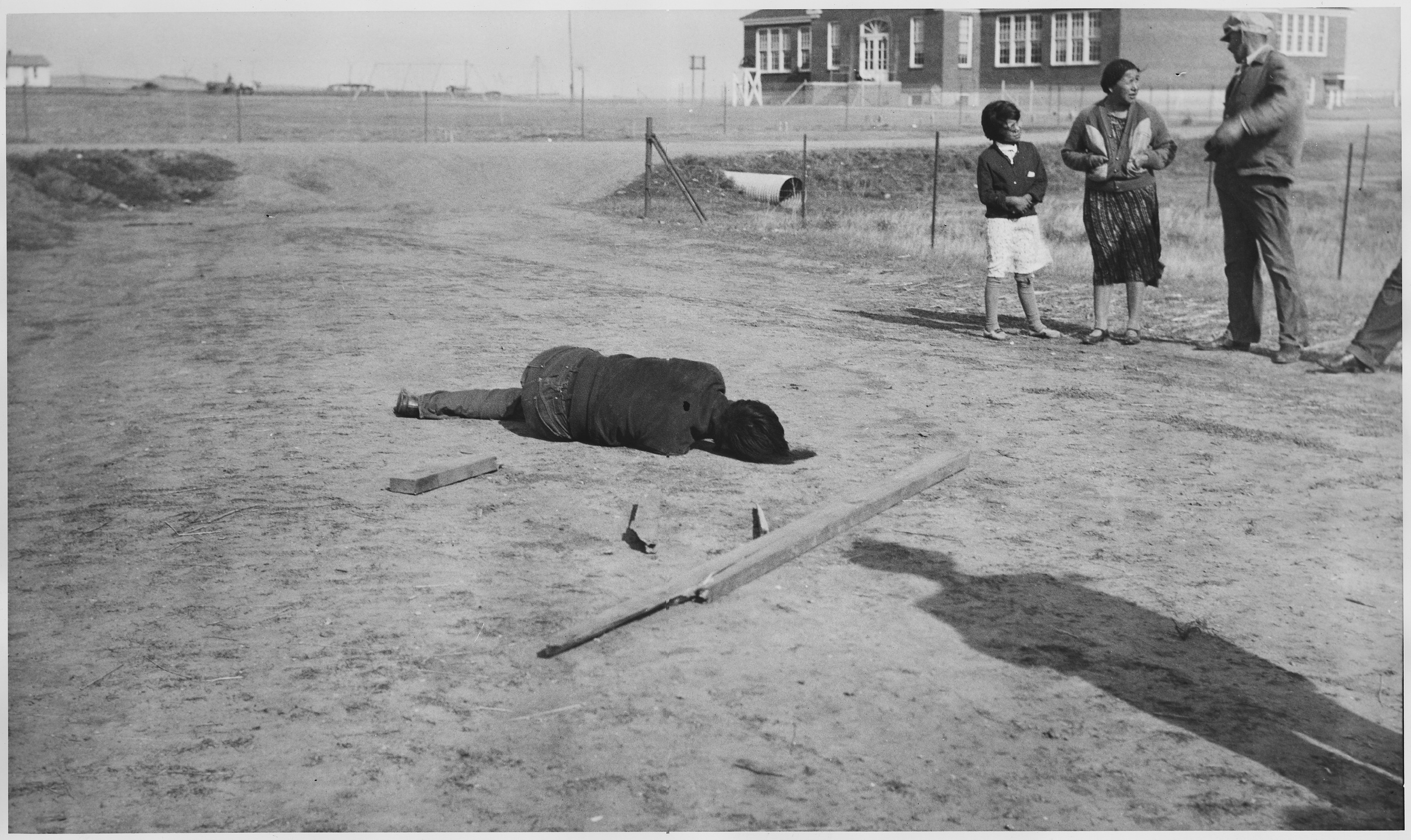 Scope and content:  The body is sprawled on ground; girl, woman, and man standing by.