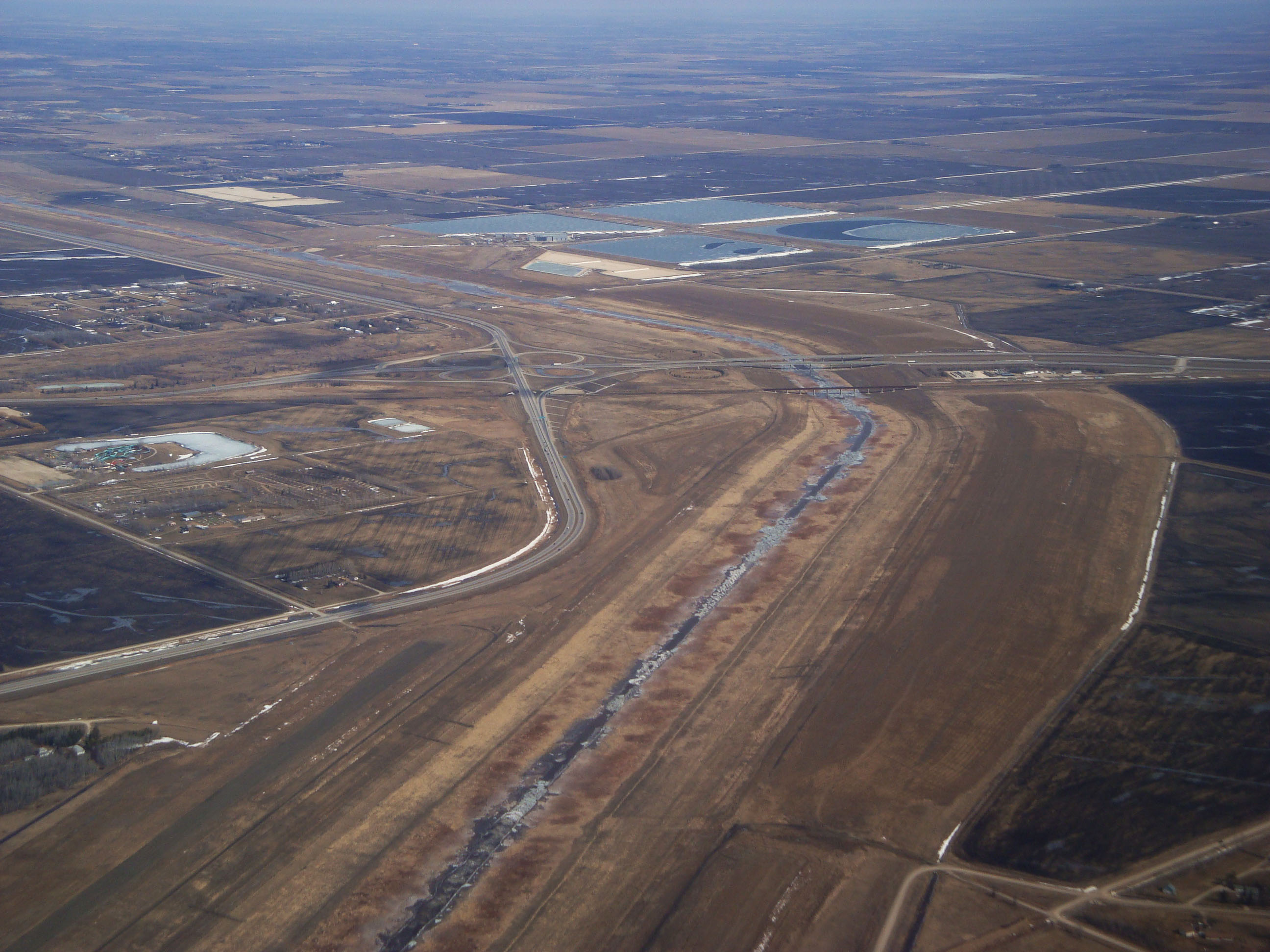 Red River floodway at the southeast corner of the Winnipeg city limits near Lorette as seen from the air. The Trans Canada Highway and Canadian National Railway bridges over the floodway can be seen, along with the Perimeter Highway.