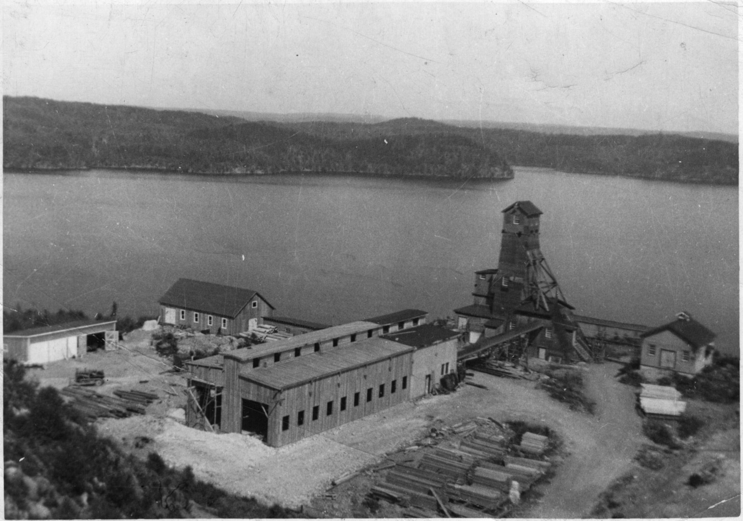 Steep Rock Lake is in the background before it was drained. The No.1 shaft is the tall building on the shore of the lake. In the foreground, the mine shop and buildings are clustered together.
