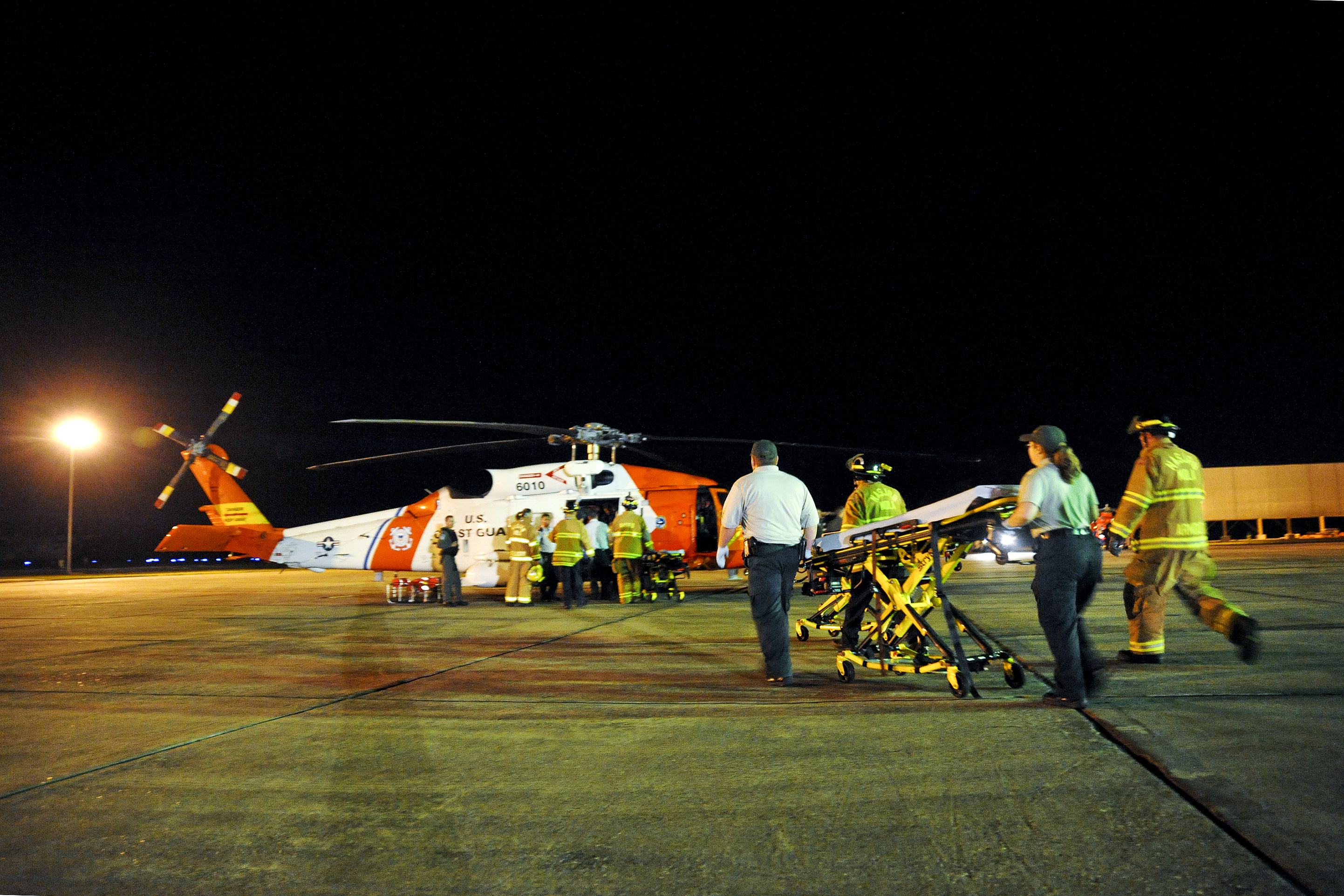 Emergency medical technicians rush a gurney to an awaiting HH-60 rescue helicopter and crew from Coast Guard Aviation Training Center Mobile, Alabama, on Coast Guard Air Station New Orleans. The helicopter crew medevaced multiple survivors from the mobile offshore drilling unit Deepwater Horizon after an explosion and fire caused the crew of the vessel to evacuate.