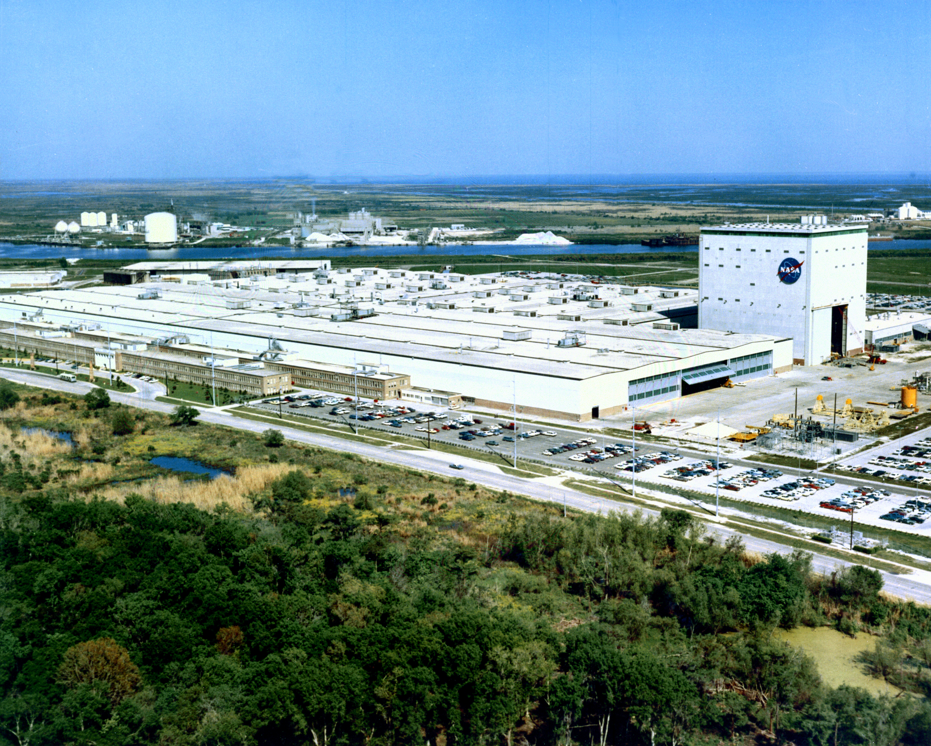 An aerial view of the manufacturing area at Michoud Assembly Facility (MAF). MAF is located 15 miles East of downtown New Orleans, Louisiana, with approximately 156 square miles of manufacturing floor space. The prime contractors, Chrysler and Boeing, manufactured the stages of Saturn IB and Saturn V during the Apollo program. Prime contractor, Lockheed Martin, manufactured the Space Shuttle External Tank (ET) during the Space Shuttle program. MAF currently manufactures the Space Launch System (SLS) and the Command Module of the Orion Multi-Purpose Crew Vehicle (Orion MPCV) under the direction of the Boeing and Lockheed Martin, respectively. This photograph was taken in 1968. View shows Facility fronting Gentilly Road, with the preserved smokestacks from the old Michoud Plantation visible in front at left. Beyond the facility the Gulf Intracoastal Waterway canal can be seen.