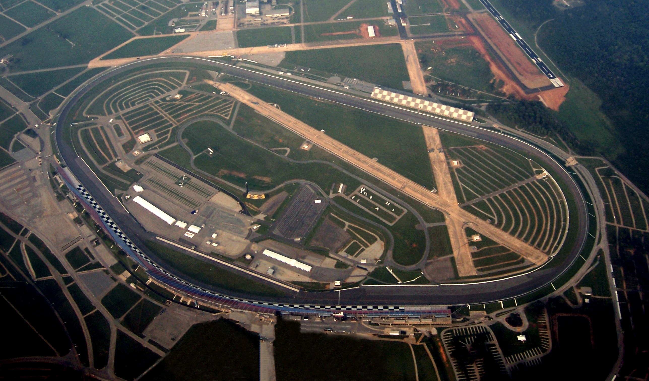 This image is of the Talladega Superspeedway, located in Talladega, Alabama. The image was taken from approximately 5000ft MSL (4500ft AGL) with visibility limited to approximately 4sm due to haze. The left wheel of the aircraft has been digitally removed from the image, causing some distortion in the lower sections, just below the track. The old w:Talladega Municipal Airport runways are still visible, crossing inside the track. The new airport and runway are located in the background, just north east of the track's position.