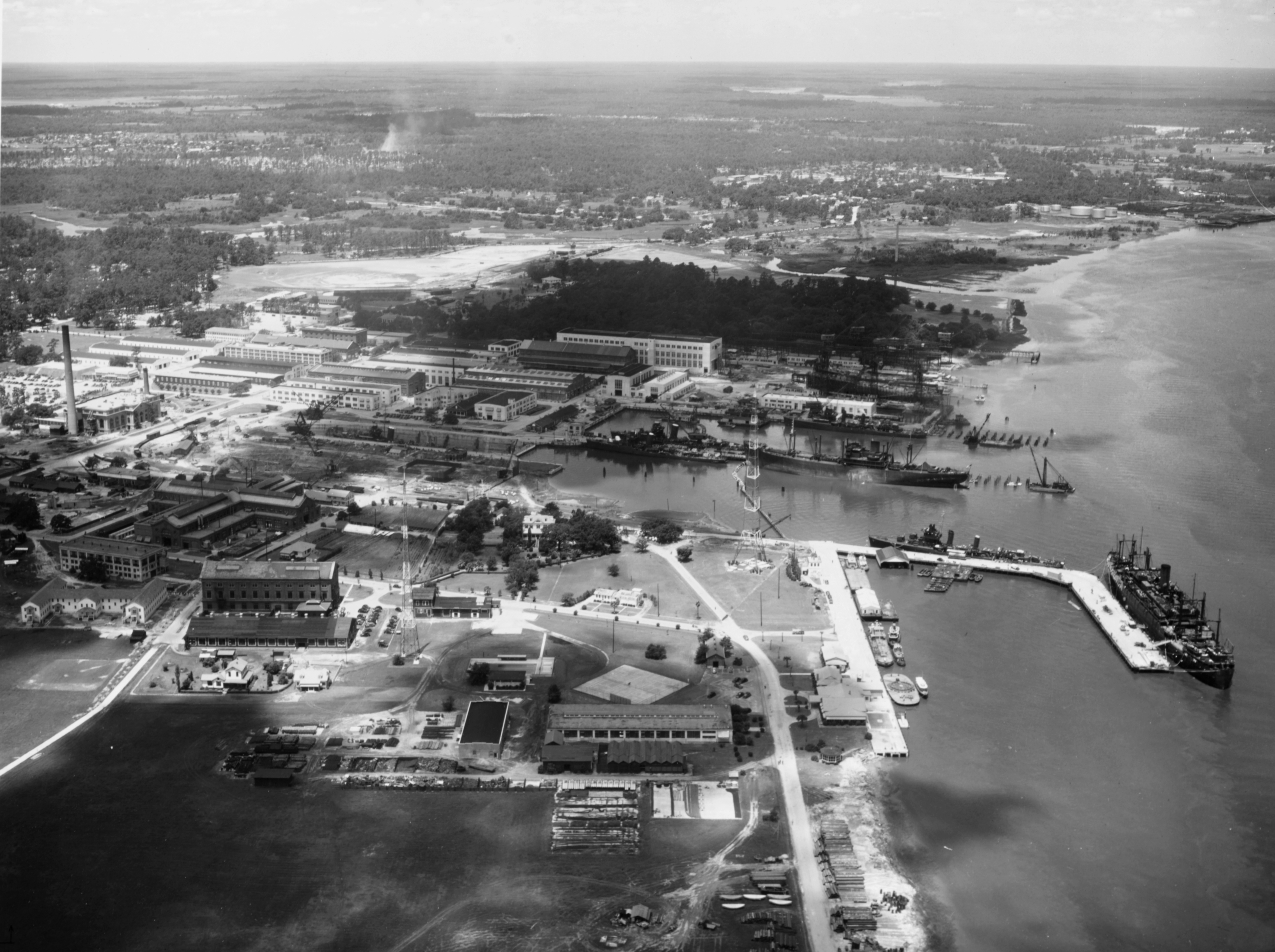 The U.S. Charleston Naval Shiyard, South Carolina (USA), preparing ships for war in 1941. The large ship on the right is probably USS Leonard Wood (AP-25), converting from an Army transport. The freighter is probably USS Hamul (AK-20), converting from a merchantman. The two two-stack destroyers at the piers are probably USS Swanson (DD-443) and USS Ingraham (DD-444) fitting out. The single-stack destroyers (2 pier side and 1 in dry dock) are probably USS Mayrant (DD-402), USS Trippe (DD-403), and USS Rhind (DD-404) in from neutrality patrol. The ships building on the ways just beyond the piers are probably USS Corry (DD-463) and USS Hobson (DD-464). Beyond them, barely visible are two more ships on another pair of ways, probably USS Beatty (DD-640) and USS Tillman (DD-641). Four of the ships afloat were commissioned between May and July 1941. The photo, taken at 300 meters, was dated 24 July 1941 and was probably taken slightly earlier. Note the Yard craft pier side in the foreground.