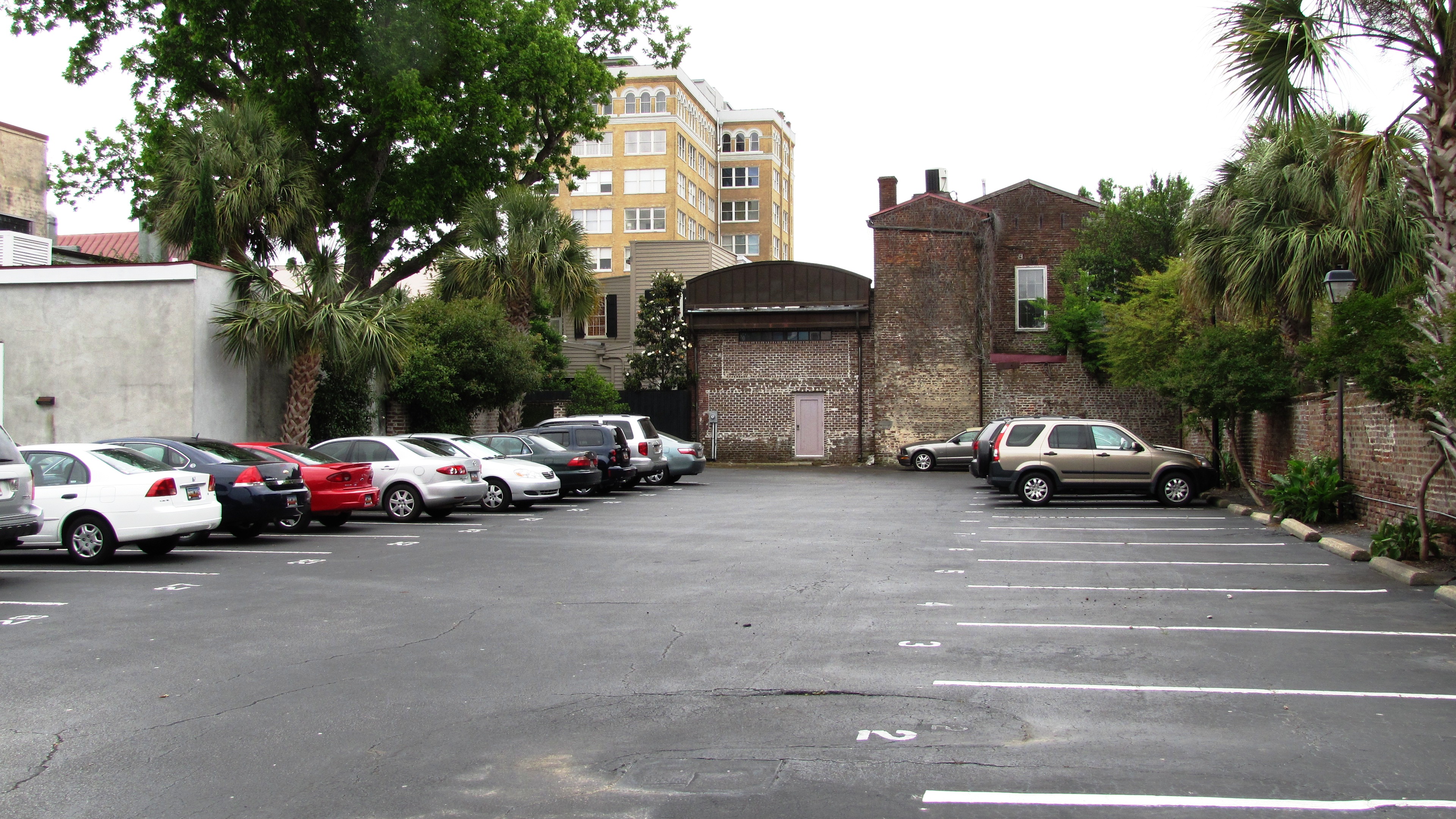Parking lot behind the Old Slave Mart (the building with the pink door near the center) that was once part of the late-1850s slave market complex known as Ryan's Mart. This view is south from where the large barracoon, or jail, once stood. The complex's kitchen was once located on the left, where the cars are parked. The complex's morgue was once located just to the right of the pink door. The auction gallery, the only extant part of the complex faces Chalmers Street.
