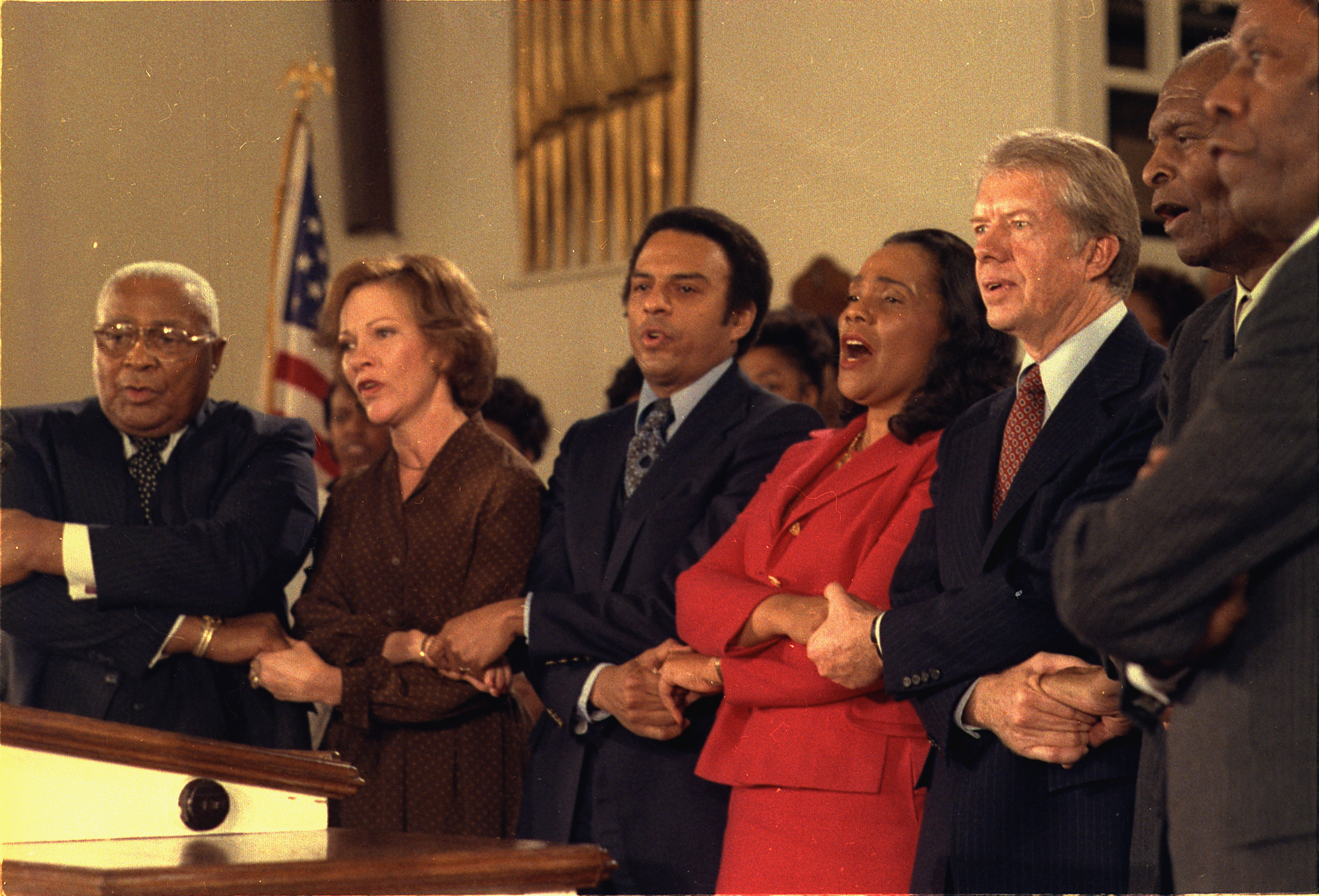 Martin Luther King Sr., Rosalynn Carter, Andrew Young, Coretta Scott King, Jimmy Carter, 2 unidentified men.  Holding hands at service at Ebenezer Baptist Church in Atlanta. 1979.