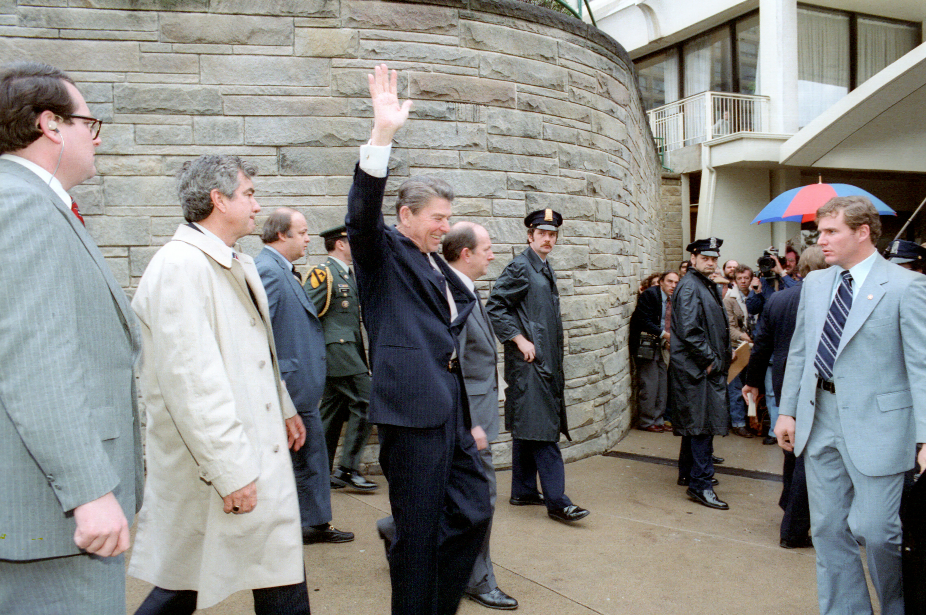 U.S. President Ronald Reagan waves moments before he was shot in an assassination attempt outside a Washington hotel on Monday, March 30, 1981. From left to right are Rick Ahearn, publicist for Reagan; secret service agent Jerry Parr, in raincoat, who pushed Reagan into the limousine; press secretary James Brady, who was seriously wounded; Jose Muratti, Reagan's military aide; Reagan; Michael Deaver, Reagan's aide; unidentified policeman; Washington policeman Thomas K. Delahanty, who was shot; and secret service agent Timothy J. McCarthy, who was shot in the stomach. Photograph ID C1426-16, ARC Identifier 198513, Collection RR-WHPO:  White House Photographic Collection, 01/20/1981-01/20/1989), Ronald Reagan Presidential Foundation and Library.