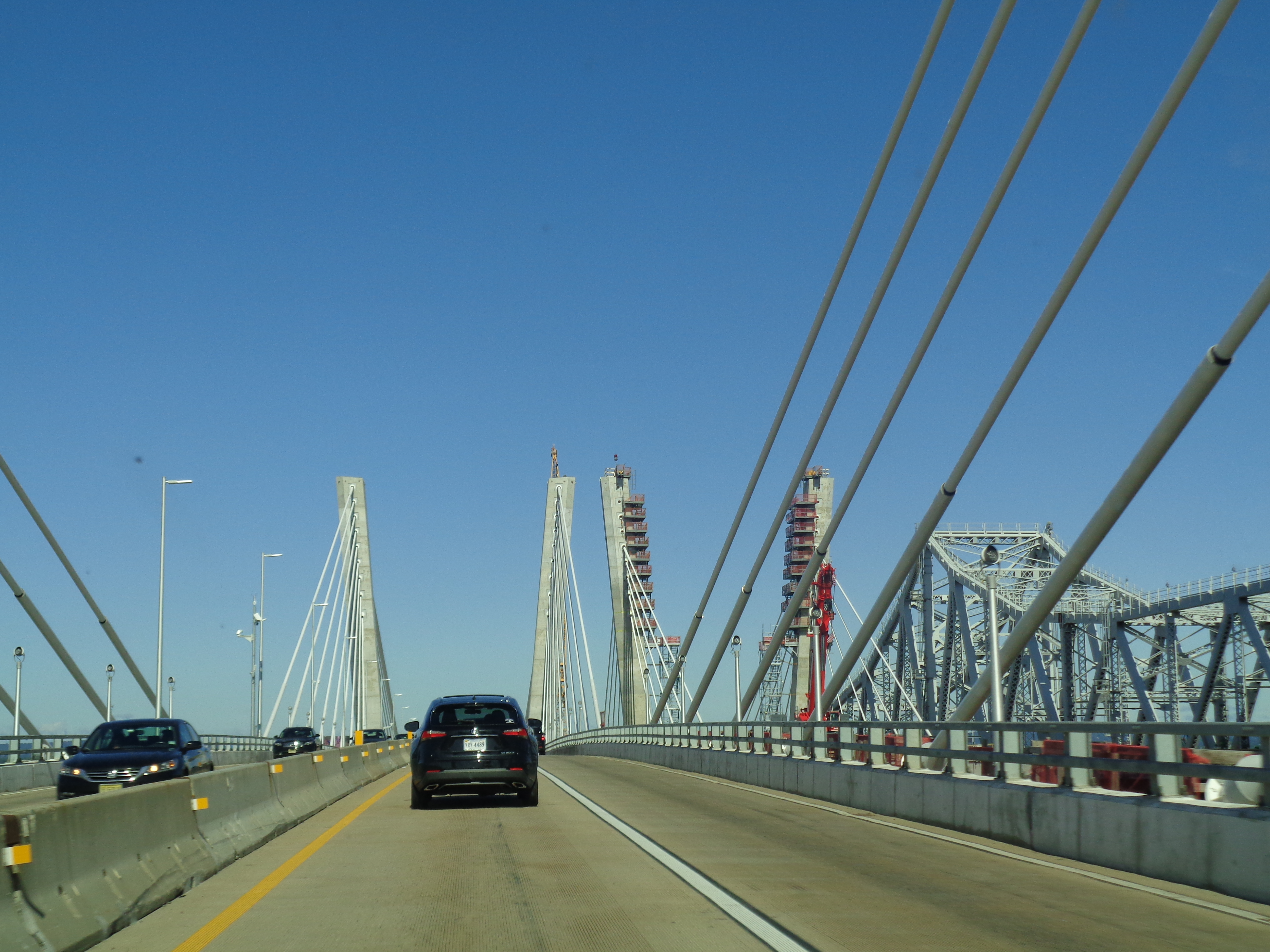 Traveling west over the eastbound span of the new Goethals Bridge between western Staten Island and Elizabeth, New Jersey. The new eastbound span, a cable-stayed bridge, is currently used for bidirectional. The new westbound span under construction and the original truss bridge are visible to the right and far right respectively.