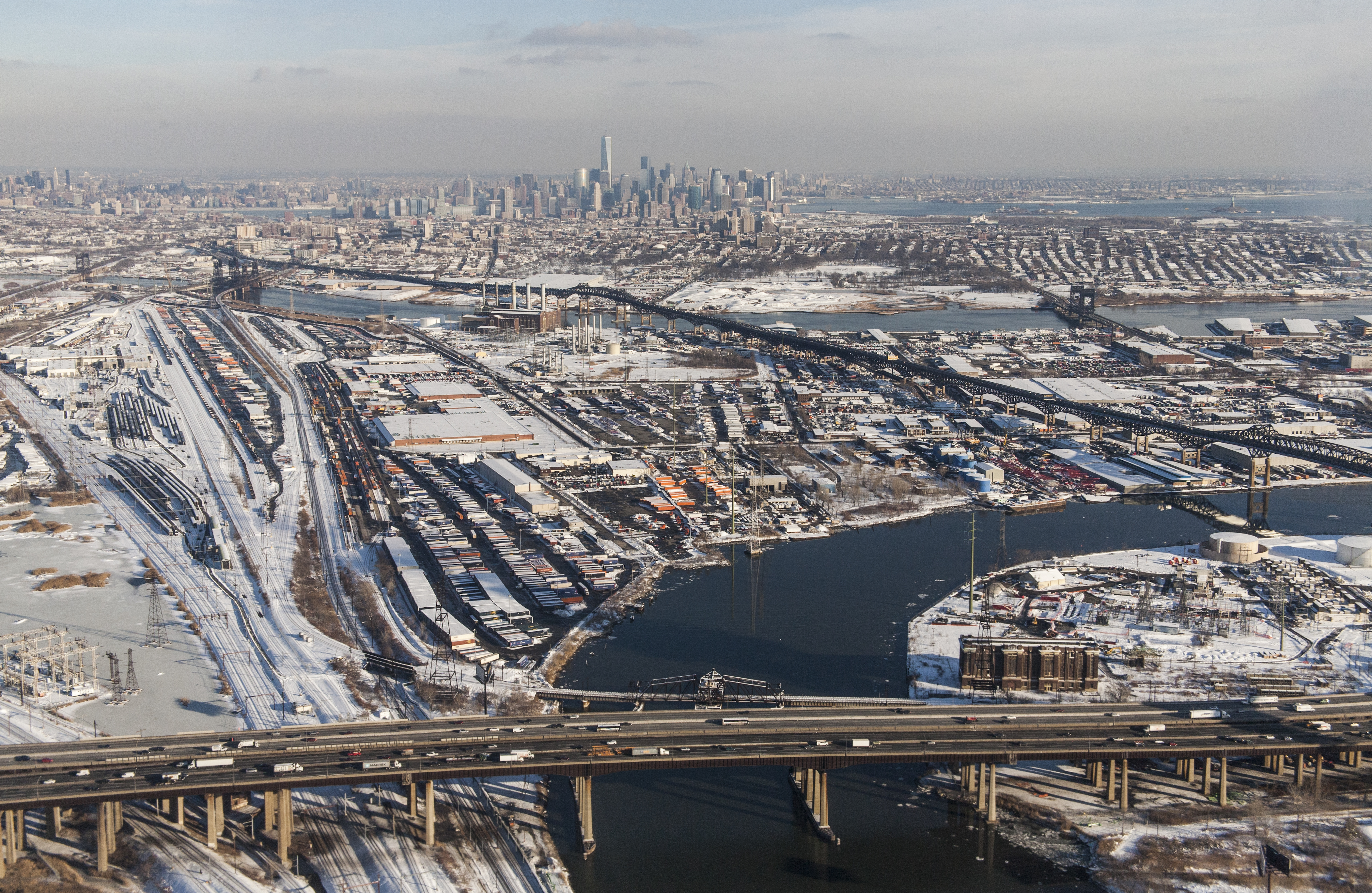 CSX South Kearny rail yard, New Jersey, with the black Pulaski Skyway (highways 1 and 9) cutting across the meadowlands below the southern Manhattan skyline, dominated by the new One World Trade Center. The New Jersey Turnpike is in the foreground, crossing the Passaic River. The Hackensack is the other river farther out. They join just offscreen to the right. The rail line on the far left, running under the Turnpike, is the Amtrak Northeast Corridor.