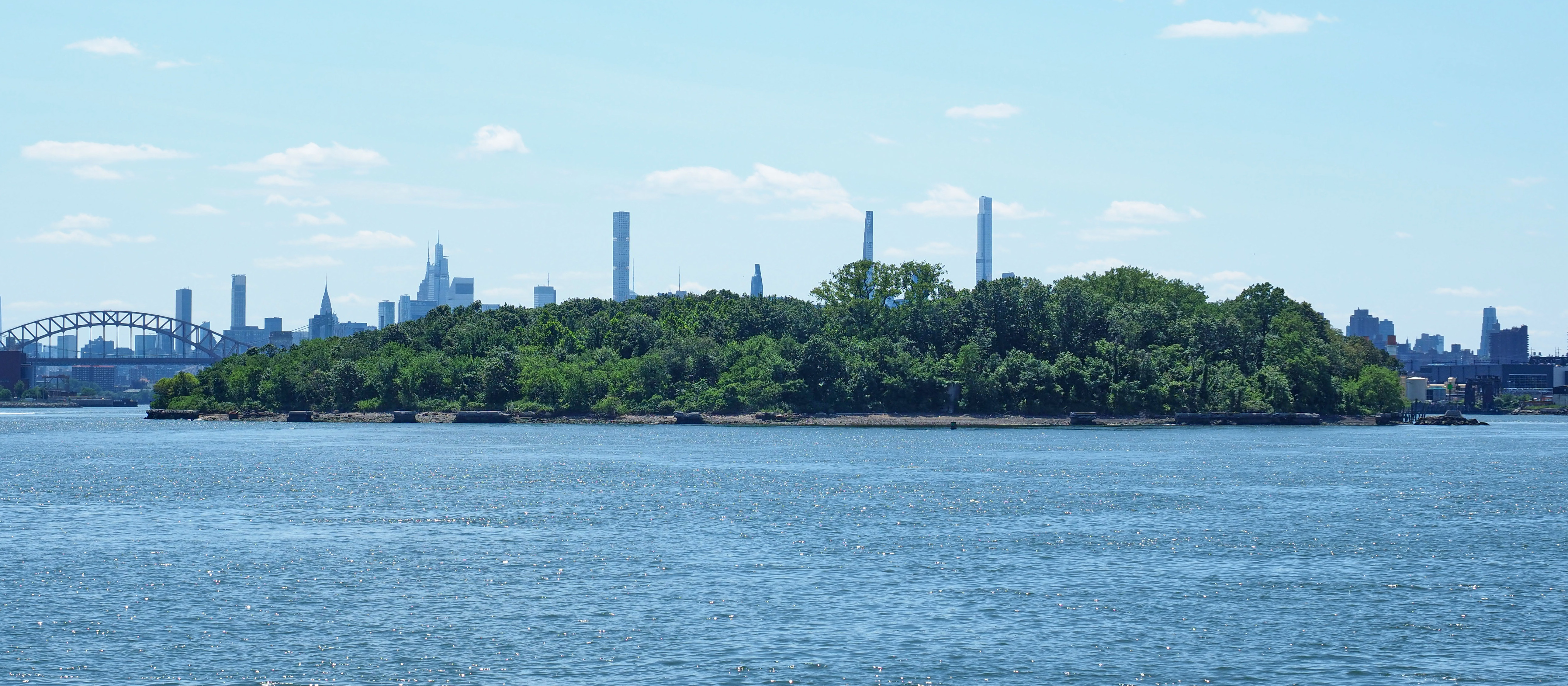 North Brother Island seen from Barretto Point Park, Bronx, New York.  Hell Gate Bridge visible at left edge of frame.  Manhattan skyline in the background.
