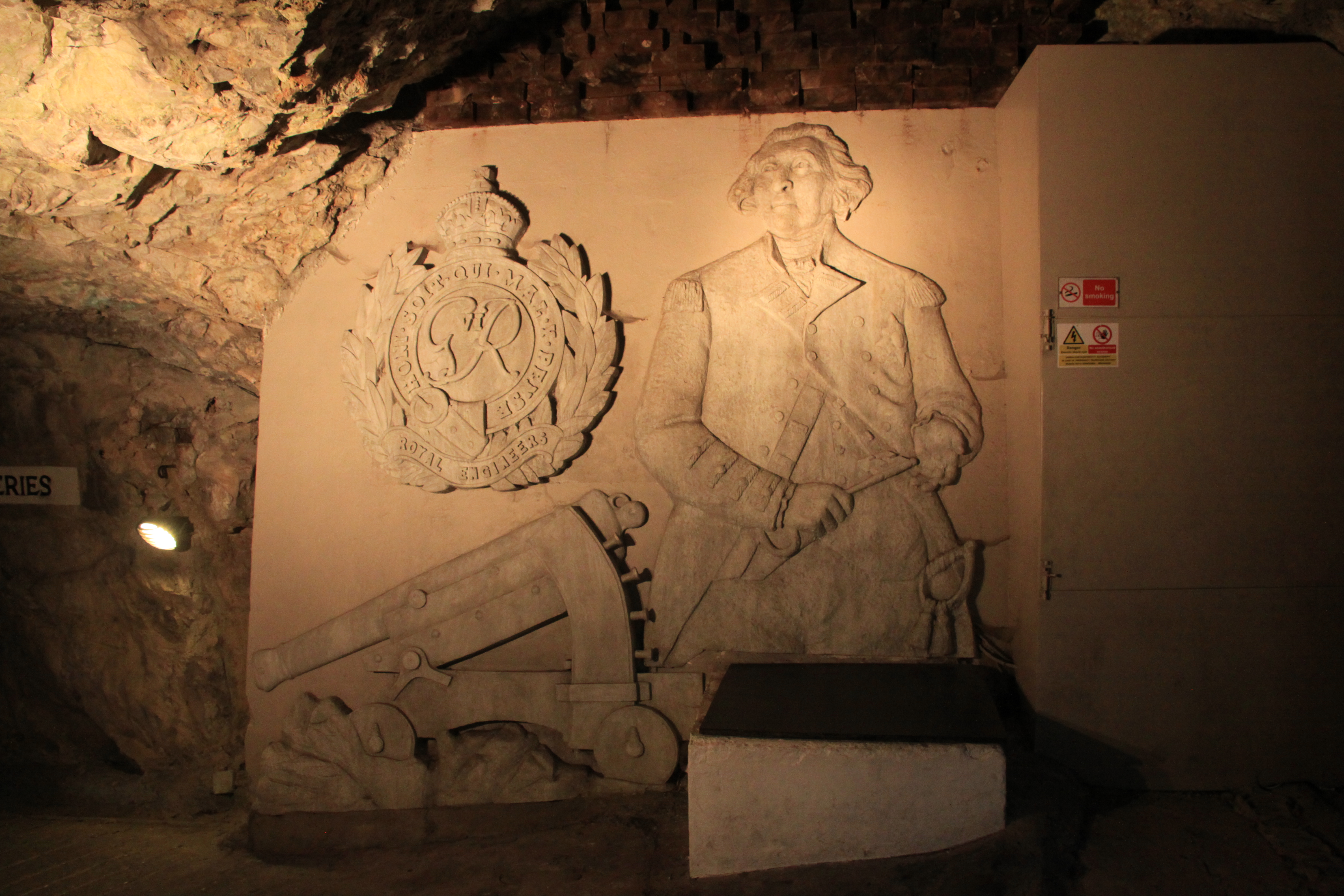 The image shows George Augustus Eliott, 1st Baron Heathfield (Governor of Gibraltar during the Great Siege) holding the Keys of Gibraltar), the crest of the Royal Engineers and a Koehler gun. It's found at the entrance to the Great Siege Tunnels in Gibraltar