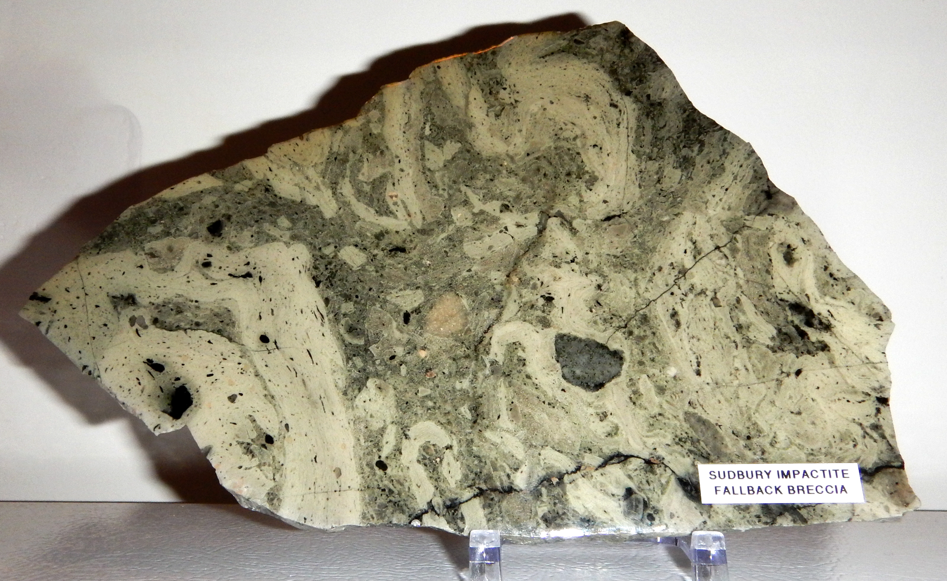 The mesmerizing impact melt of the Sudbury Impactite, from concentric rock formations outlining a large crater. The Sudbury crater was created by a big rock from space crashing into the Earth 1.87 billion years ago. The impact structure has since been pinched one way and elongated the other direction to 190 km length by plate tectonics.
The polished 9 x 6 inch slice of Grey Onaping Fallback Breccia is from Highway 144 near Dowling, Sudbury District, Ontario and sold to yours truly by the Rox Rock Shop in Westport Ontario.
Further linkage for the power and extent of the Sudbury impactor by its rattling what was the 1.87 billion year old landscape over in what is now Thunder Bay, 600 miles away.

 flic.kr/p/deHLxy