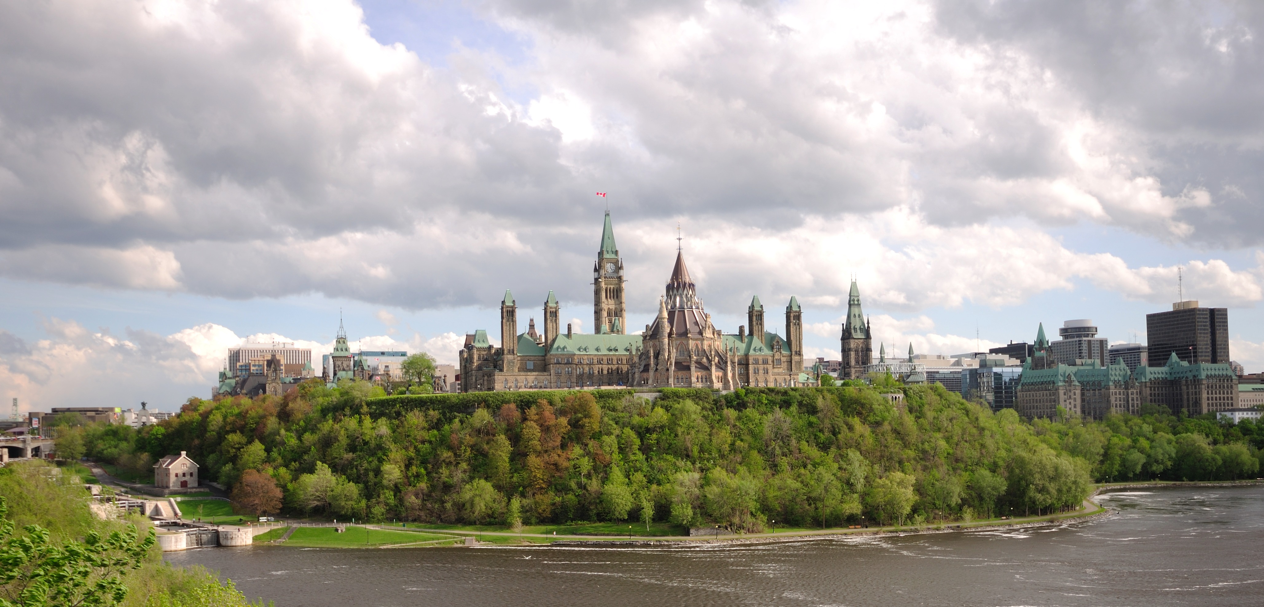 Ottawa: Stadtansicht auf den Parliament Hill vom Majors Hill Park aus, links vom Parlament erkennt man die Staustufen des Rideau Canal, rechts am Rand steht das mit 112 m höchste Gebäude der Stadt Place de Ville II