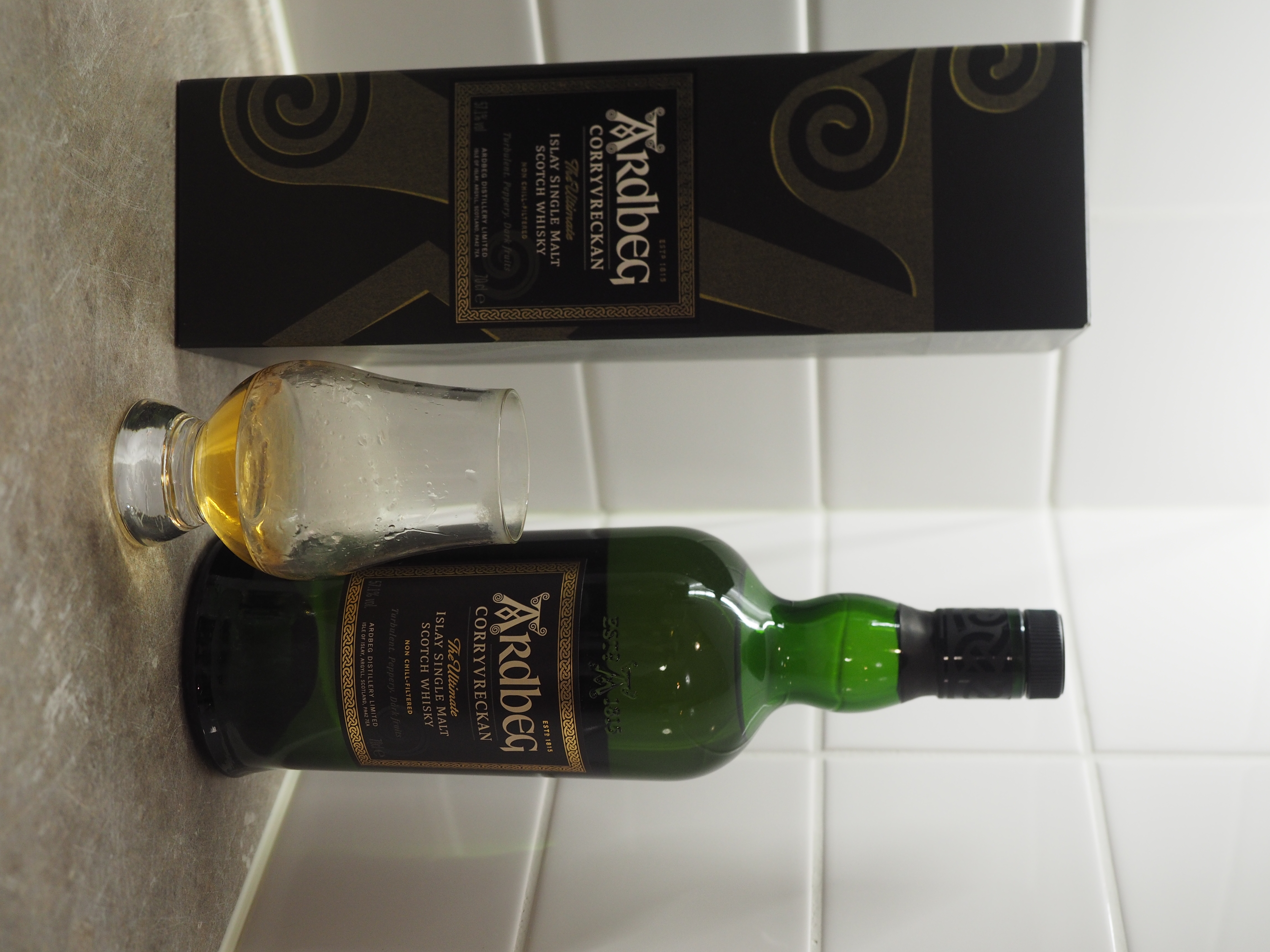 A bottle of Ardbeg Corryvreckan single malt Scotch whisky with its decorative and protective casing, with a small amount of the whisky poured into a whisky glass.