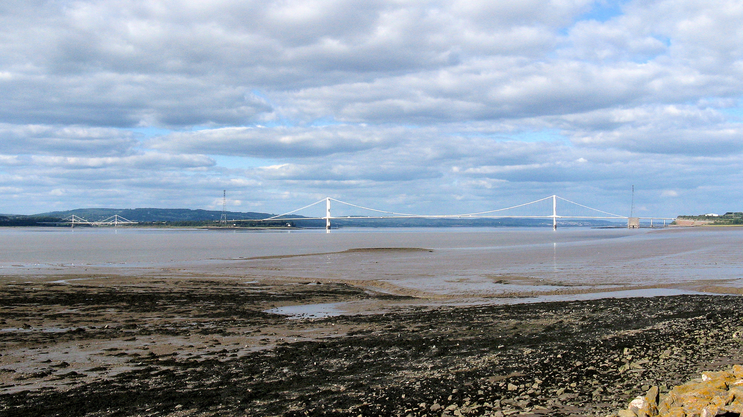 On the right the Severn Bridge crosses the River Severn. On the left  the much smaller Wye Bridge spans the River Wye. 
The Severn bridge is entirely in England - the right-hand tower is in South Gloucestershire and the other tower is in Gloucestershire.

The right-hand half of the Wye bridge is also in England (Gloucestershire). Wales starts halfway between its towers (Monmouthshire).