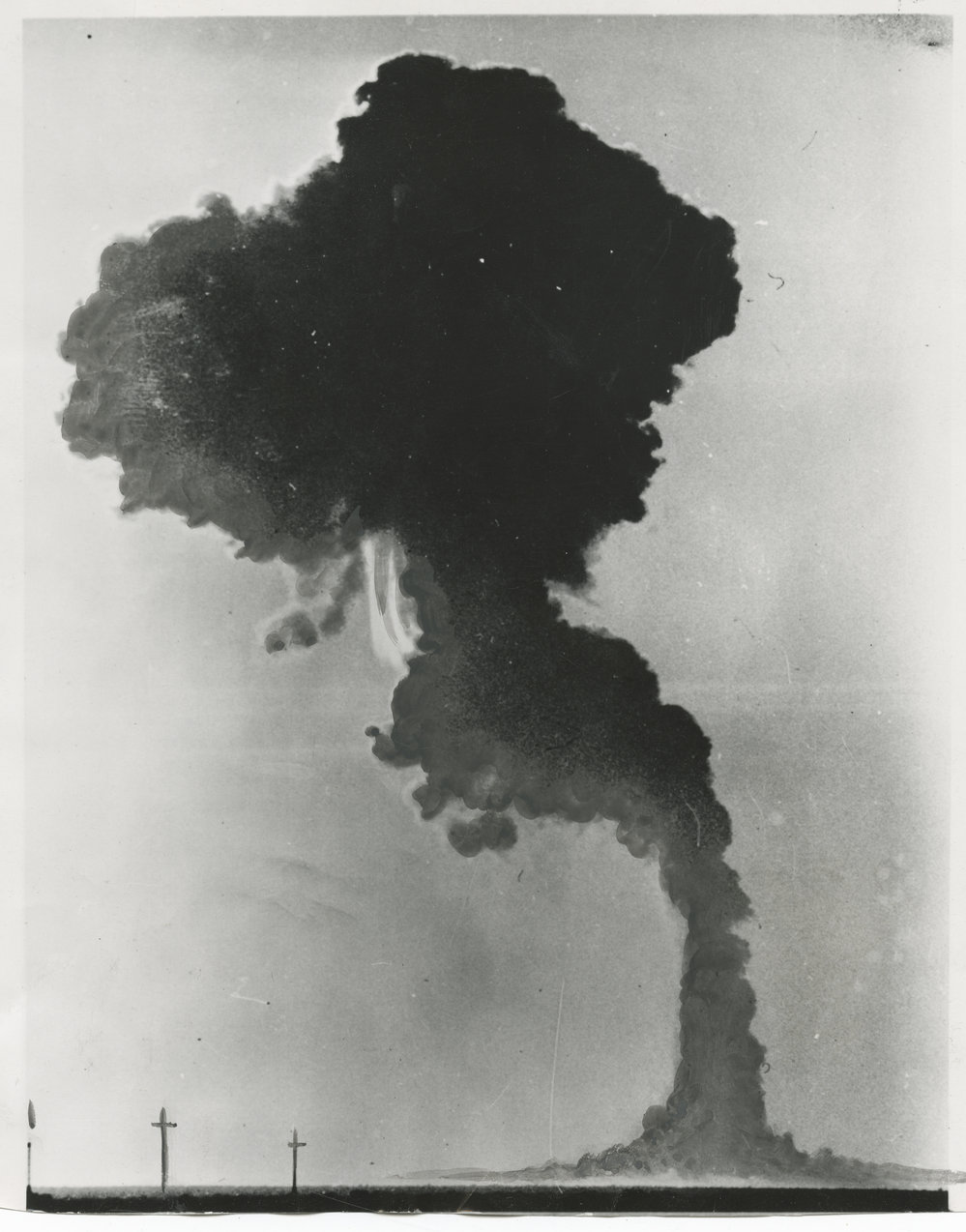 Press photograph, with grey gouache highlights, of the first nuclear test on the Australian mainland, Totem 1, which was carried out at Emu Field in the Great Victoria Desert, north-western South Australia on 15 October 1953. Verso with wet stamps dated OCT 19 1953, and pastedown newspaper clipping (from an American newspaper): 'ATOMIC CLOUD: In South Australia - A cloud formed over the Woomera rocket range after a recent atomic test conducted by British scientists. - A.P. wirephoto