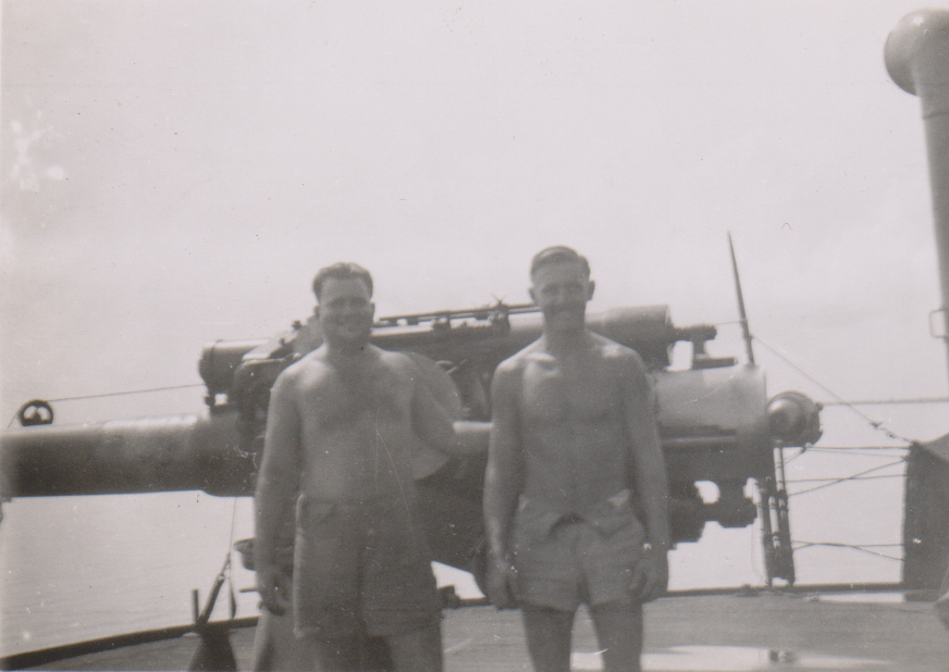Two Australian Merchant Navy sea men standing in front of a gun onboard a ship during World War II