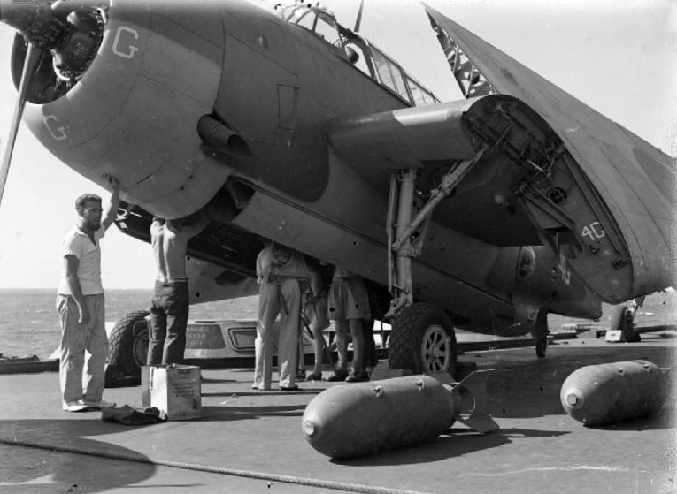 Bombing up a Royal Navy Grumman Avenger Mk.II aircraft of 832 or 845 Naval Air Squadron on the flight deck of the aircraft carrier HMS Illustrious (87) sailing in the Indian Ocean in readiness for the raid on Soerabaya, Java, in May 1944. The air strike against the Japanese held naval base was carried out by British, American, Australian, French and Dutch units. Several of the armourers are stood inside the aircraft's open bomb bay.