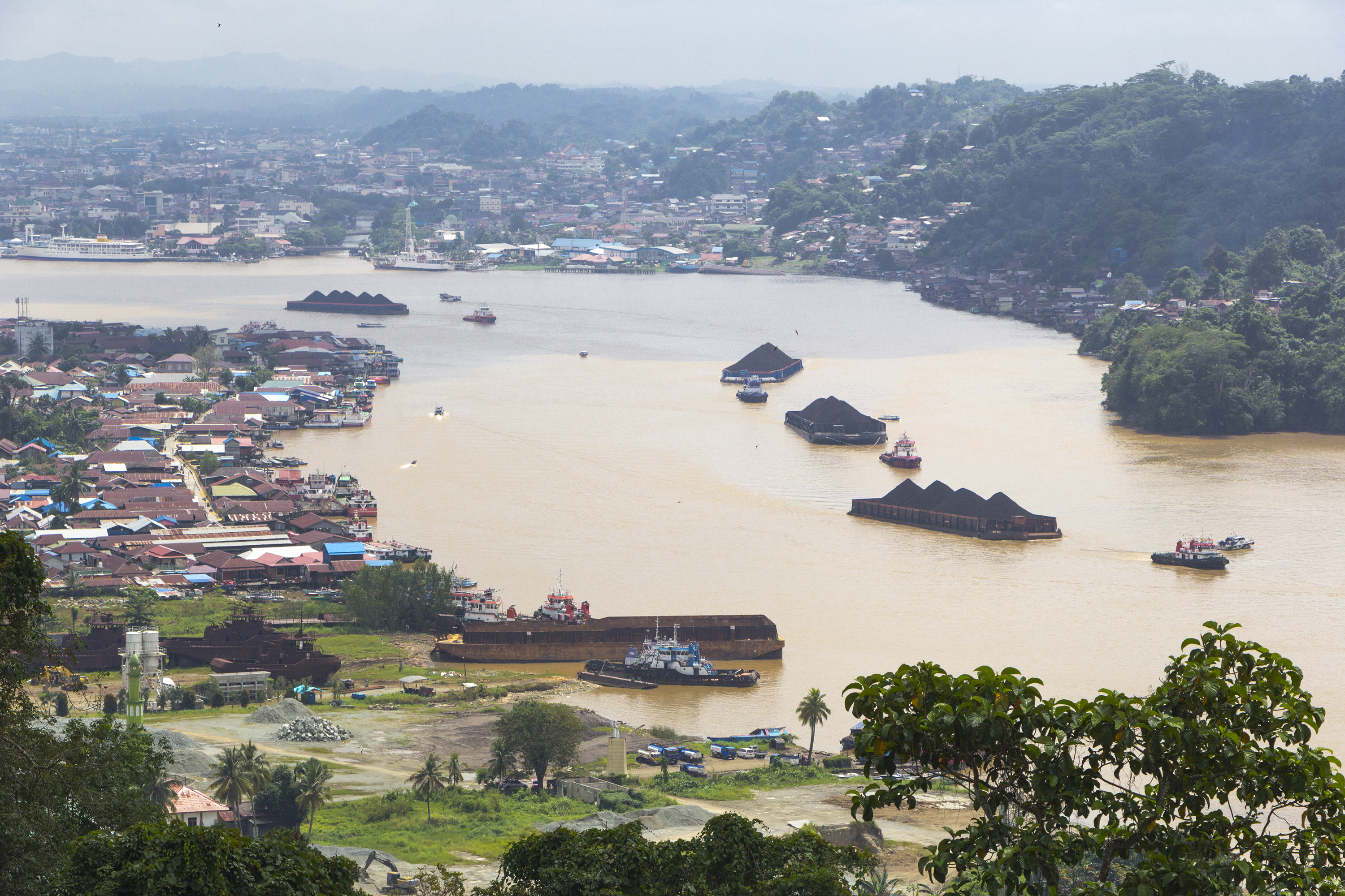 Barges with large tonnage loaded with coal and other goods pass by on the Mahakam river, Samarinda City, Indonesia.