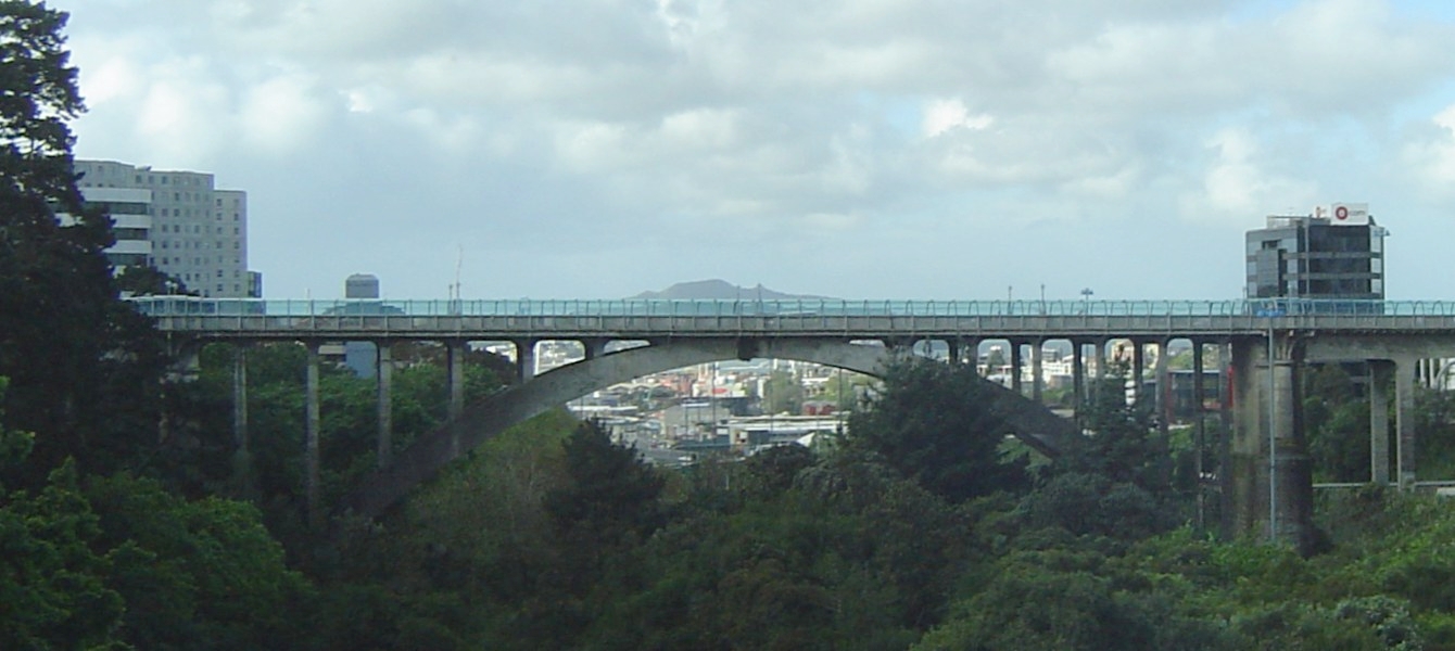 Grafton Bridge, Auckland City, New Zealand. Seen from the south, looking over Grafton Gully towards Rangitoto Island (rising just above the arch). Taken from a moving car, but in my defense, it was on a slow-moving on-ramp...