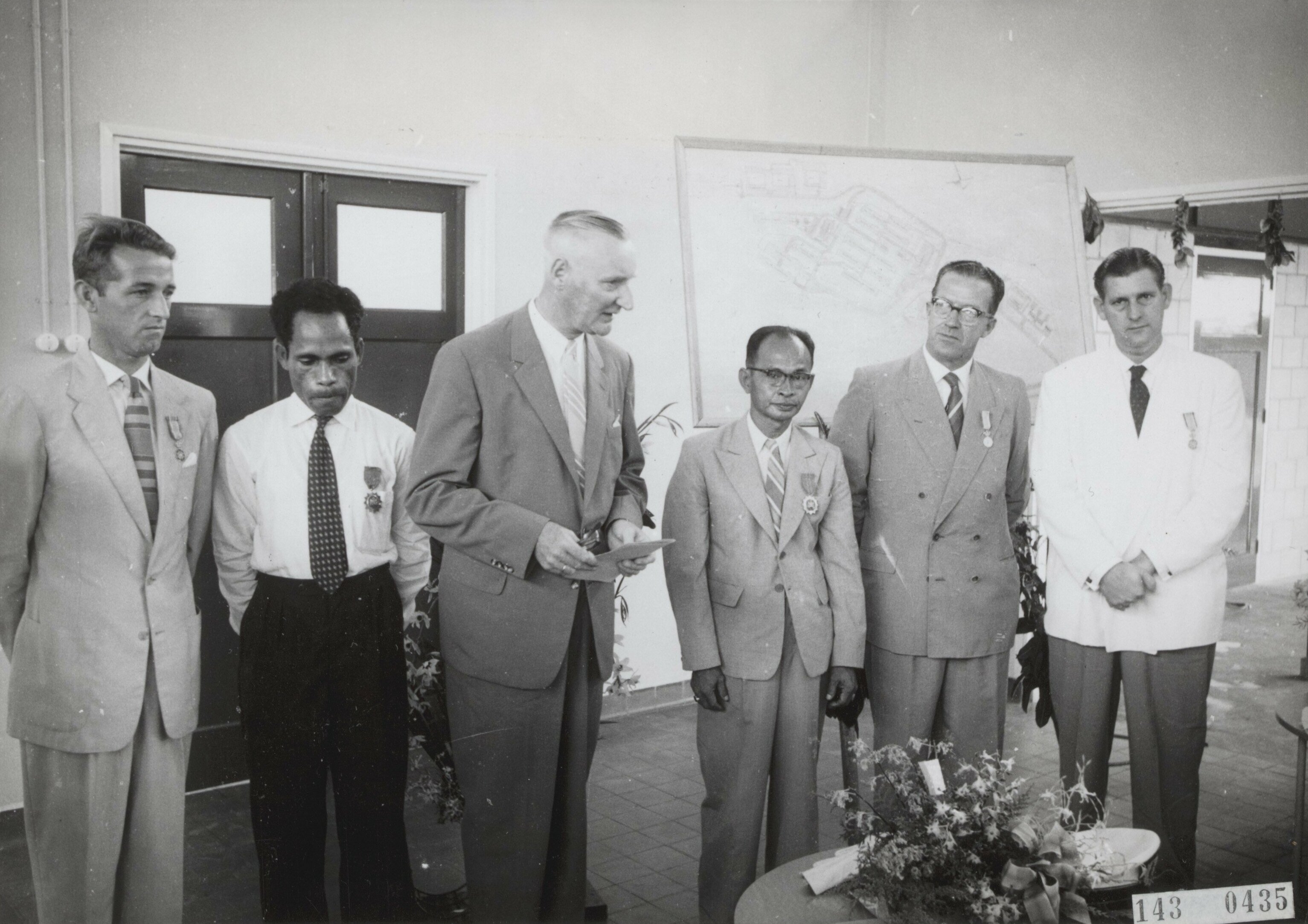 Opening Centraal Ziekenhuis te Hollandia - Nederlands Nieuw Guinea: Uitreiking decoraties. Van links naar rechts: 1. men. Petersen, Opzichter bouw Ziekenhuis (in dienst van het Gouvernement): Koninklijke Onderscheiding, 2. men. Rumainum: Onderscheiding van het Gouvernement, 3. men. Zuiderhoek: Hoofd Dienst van Volksgezondheid houdt toespraak, 4. men. Mandosir: Onderscheiding van het Gouvernement, 5. men. ? : Uitvoerder (in dienst van samenwerkende bouwonderneming): Koninklijke Onderscheiding, 6. men. Gerrit Palsgraaf: Hoofduitvoerder Bouwmij Hollandia BMH: Koninklijke Onderscheiding.