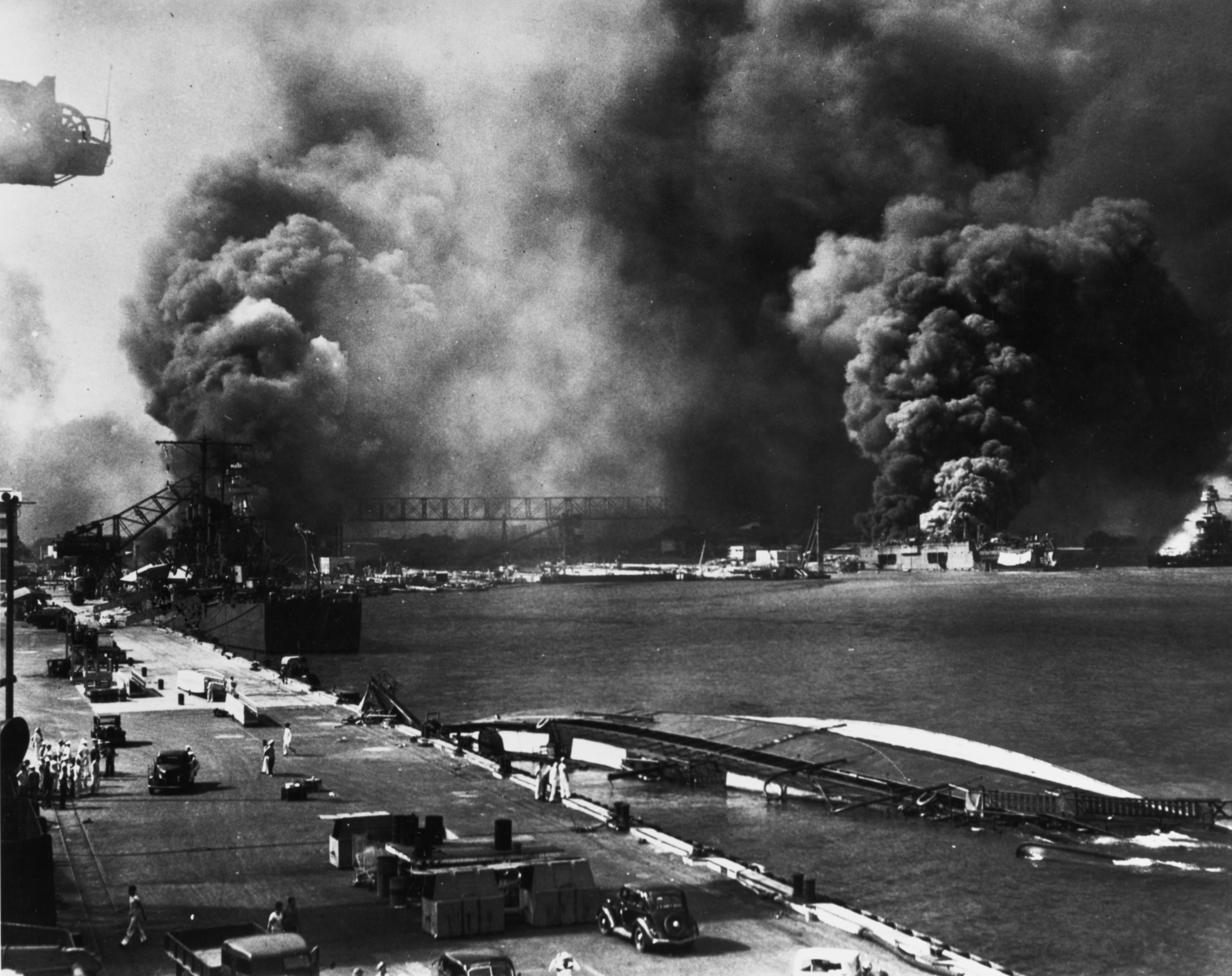 Pearl Harbor Attack, 7 December 1941: View from Pier 1010, looking toward the Pearl Harbor Navy Yard's drydocks, with the destroyer USS Shaw (DD-373) in floating drydock YFD-2 and the battleship USS Nevada (BB-36) burning at right. In the foreground is the capsized minelayler USS Oglala (CM-4), with the light cruiser USS Helena (CL-50) further down the pier, at left. Beyond Helena is Drydock No.1, with USS Pennsylvania (BB-38) and the burning destroyers USS Cassin (DD-372) and USS Downes (DD-375).