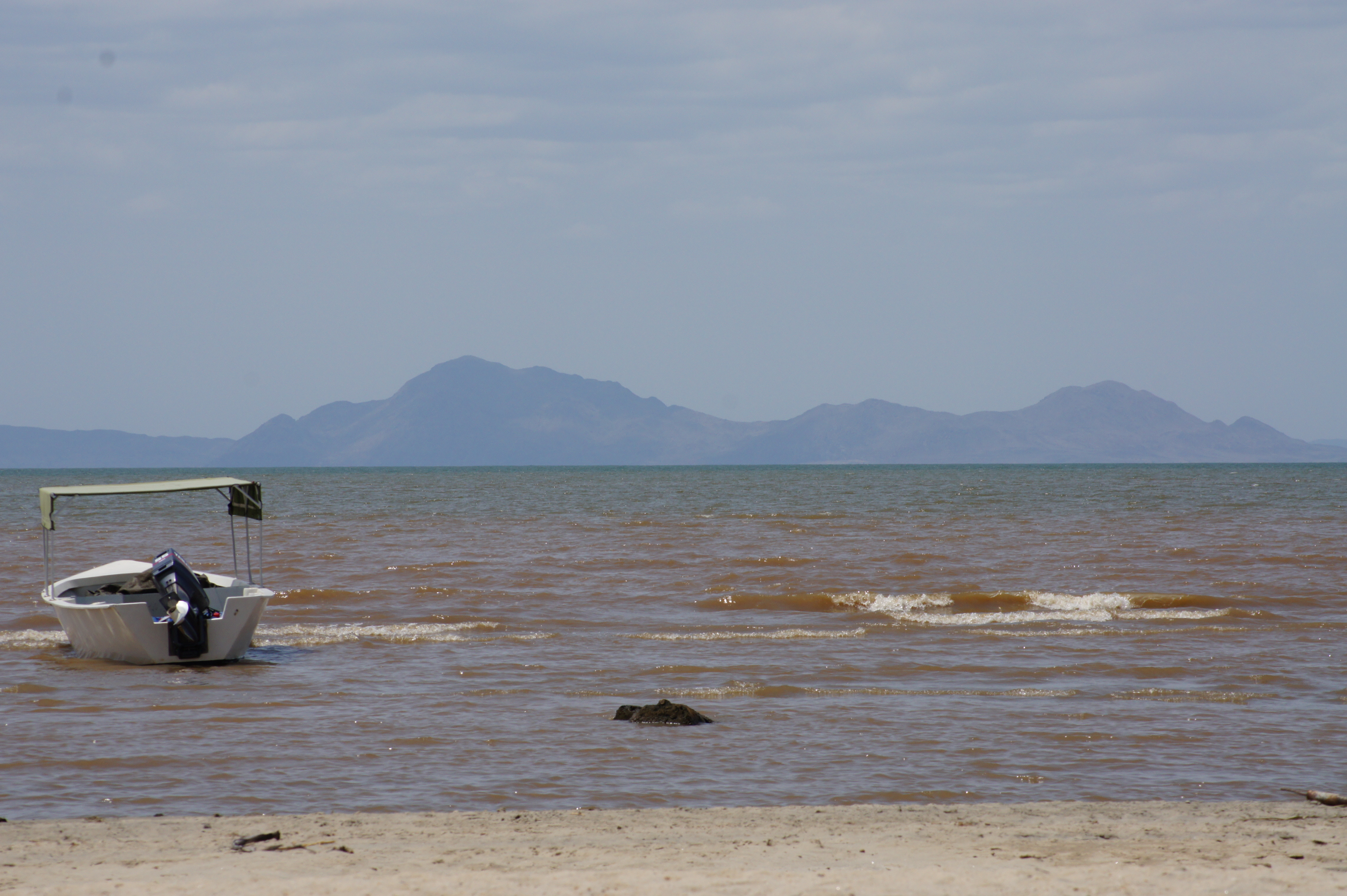 A view of Lake Turkana in Kenya with a boat in foreground and mountains in the background.